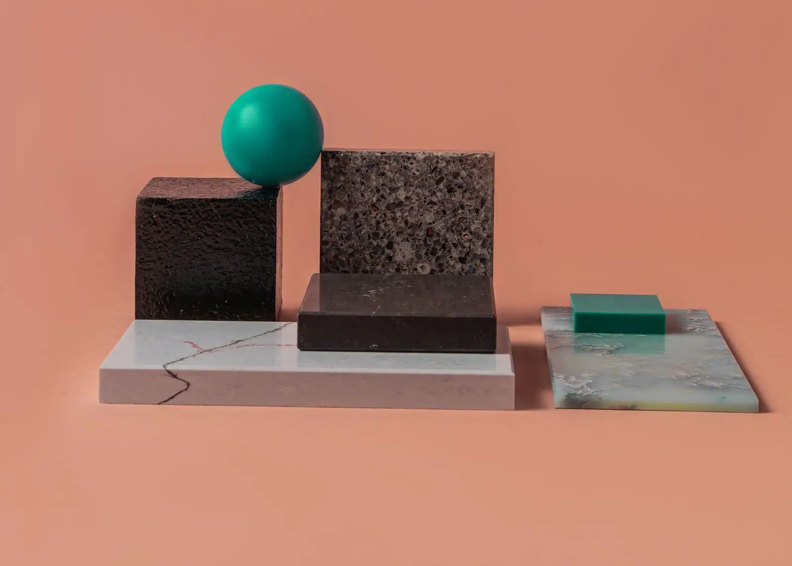 Échantillons de matières aux textures variées — pierre, marbre, surfaces mate et brillante — sur fond rose