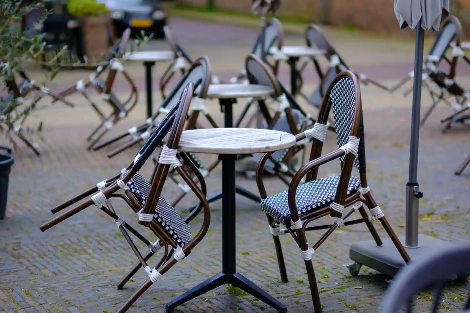 Terrasse de café avec chaises de bistrot en rotin et tables rondes sur une rue pavée