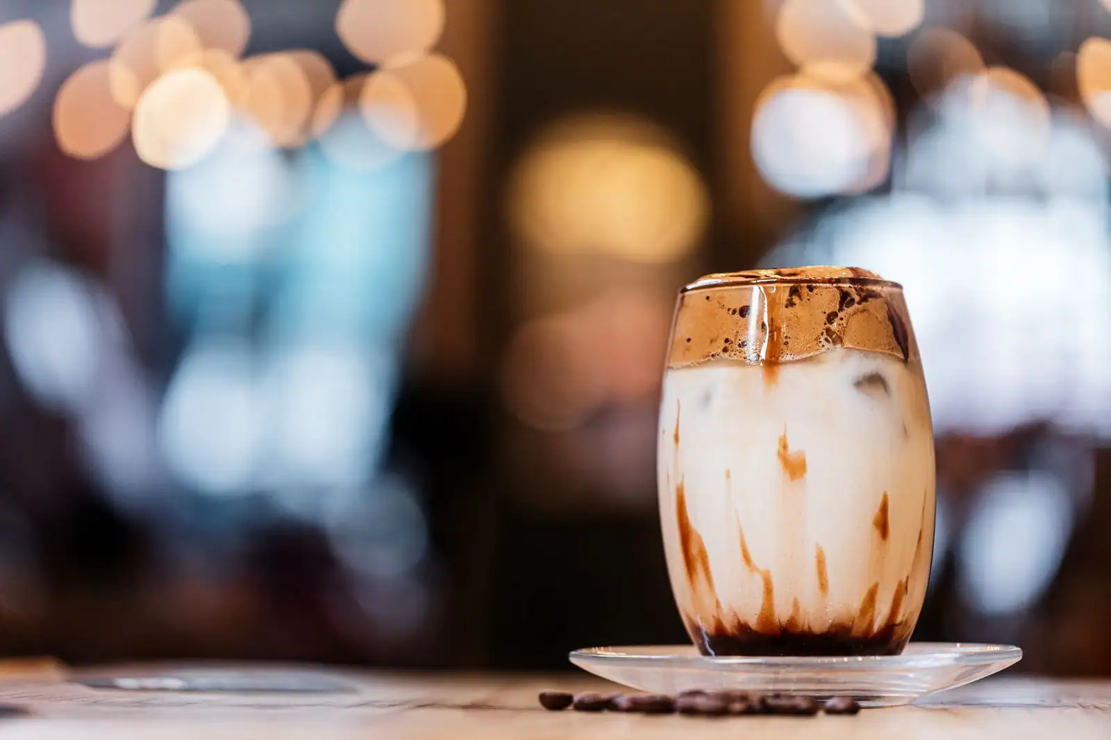 Café frappé glacé dans un verre avec lait, glaçons et mousse de café, grains de café à côté