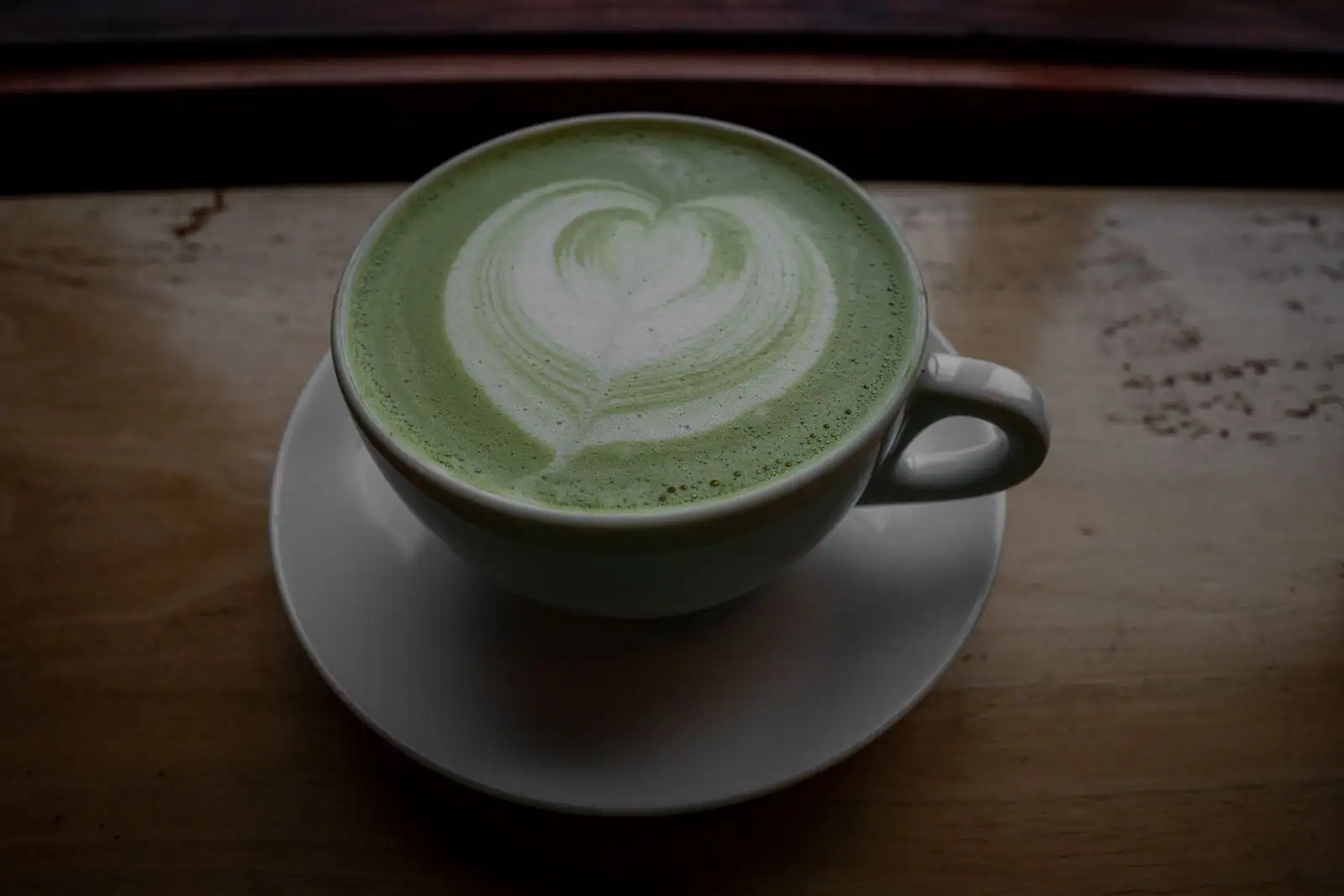 Matcha latte au lait moussé orné d'un cœur en latte art, dans une tasse blanche sur une table en bois.