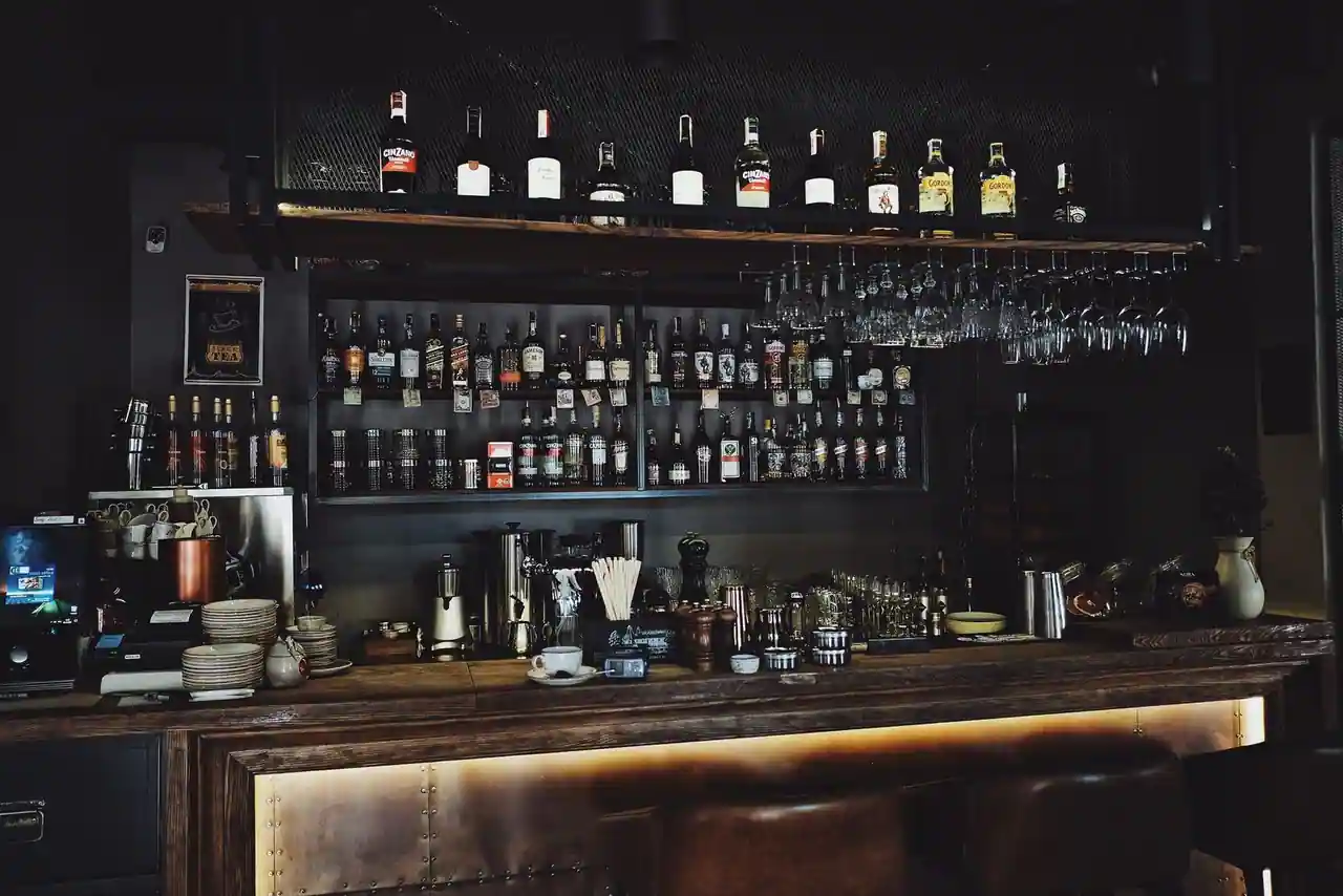 Comptoir de bar en bois avec étagères de bouteilles et verres suspendus, ambiance tamisée