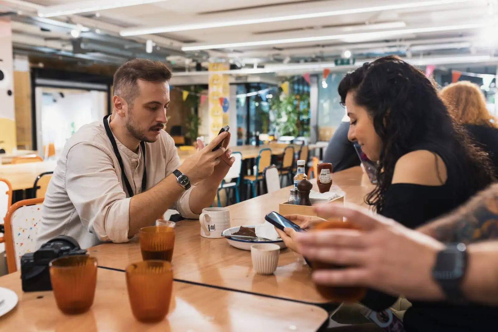Jeunes adultes attablés à un grand comptoir en bois dans un café convivial, tasses de café posées