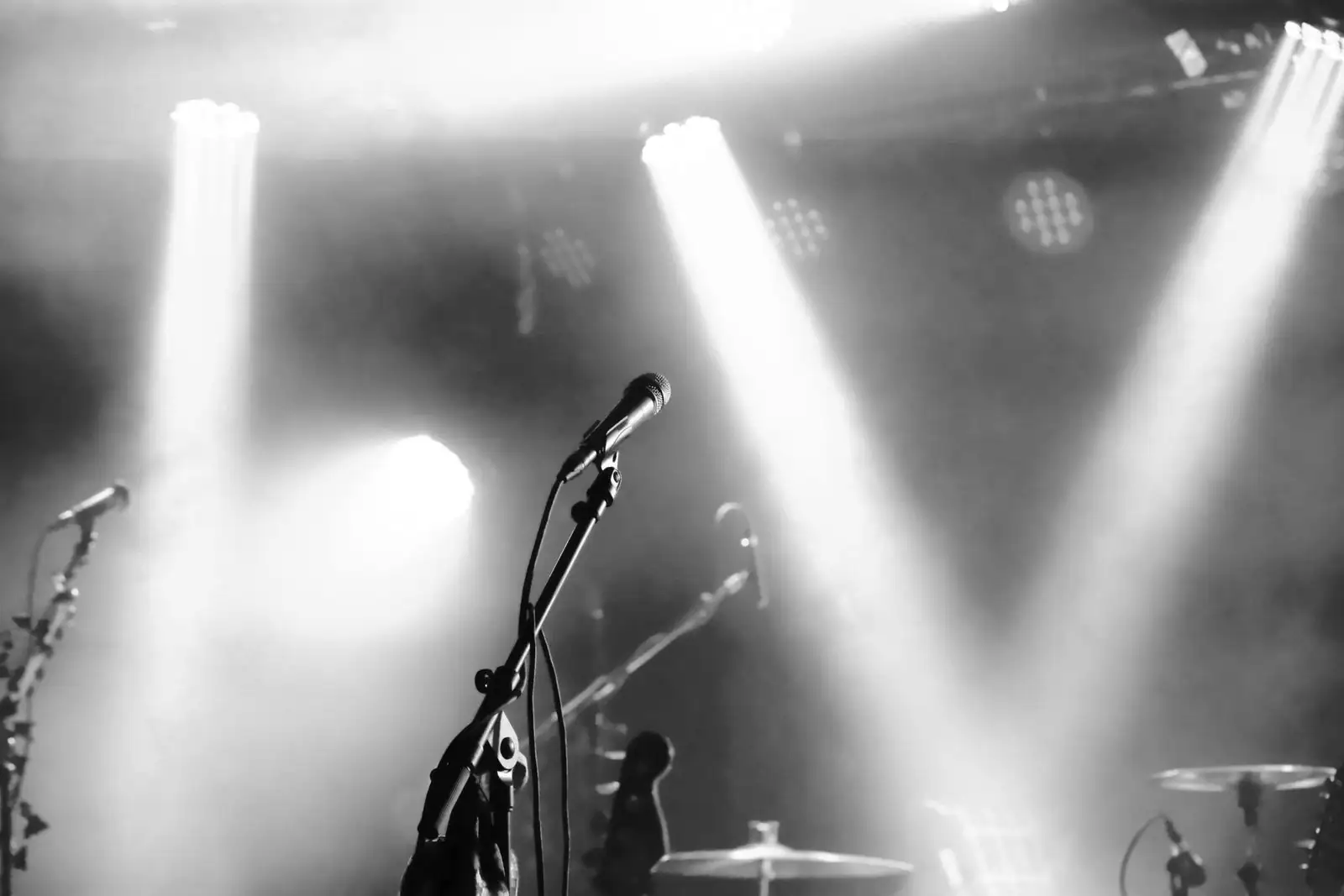 Micro de chant sur pied sur une scène de concert en noir et blanc, balayée par les projecteurs.