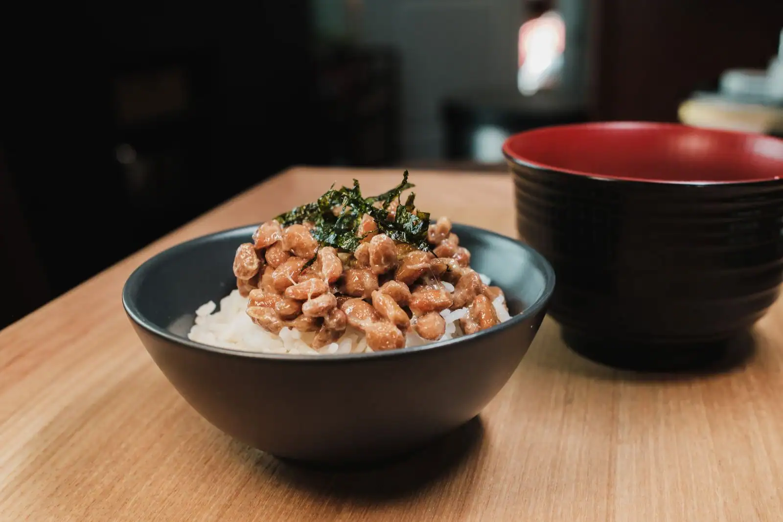 Bol de riz japonais garni de natto et de nori, posé près d'un bol à soupe traditionnel