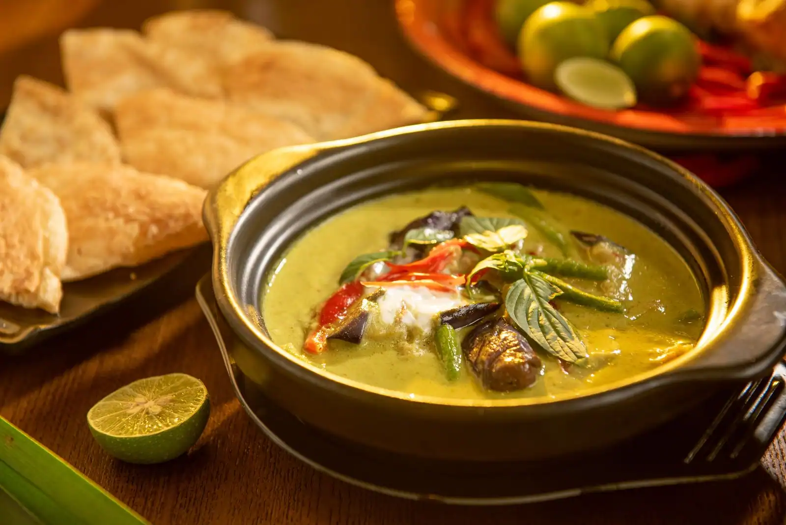 Curry vert thaïlandais au lait de coco, garni de basilic thaï, de piment rouge et d'aubergines, servi en cocotte.