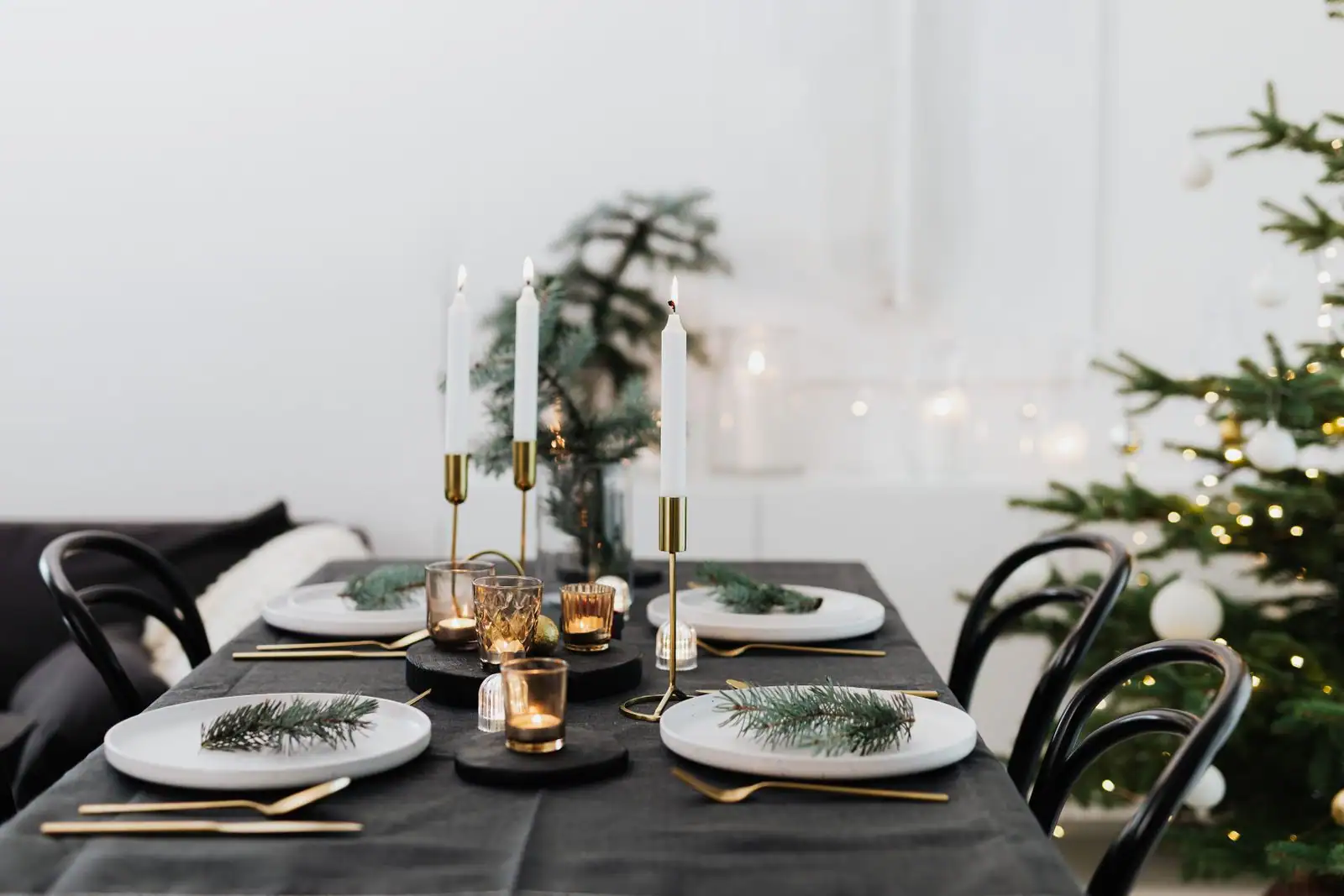 Table de Noël : assiettes blanches ornées de branches de sapin, couverts dorés et bougies blanches.