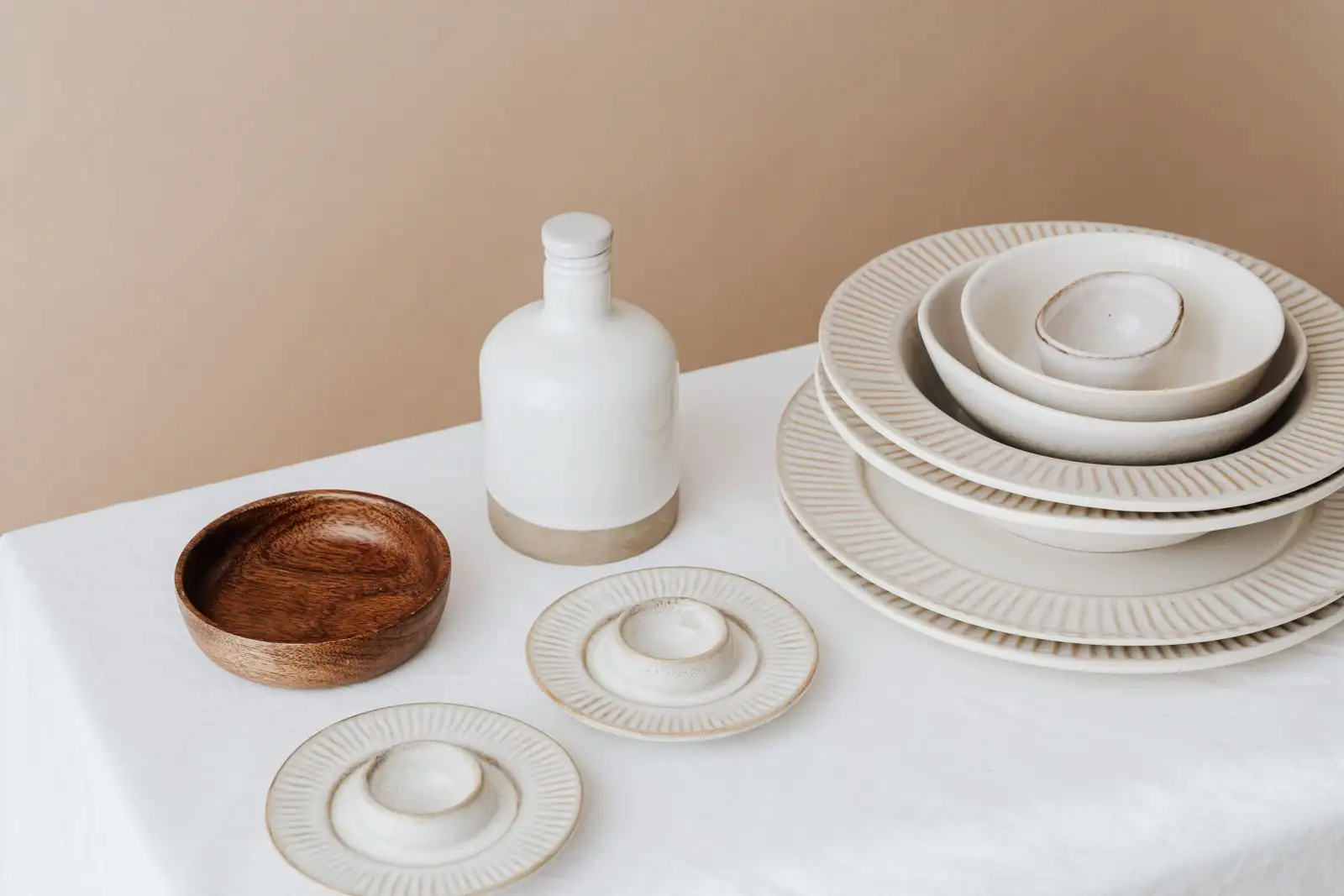 Vaisselle en céramique aux tons neutres, assiettes et bols empilés sur une nappe en lin clair