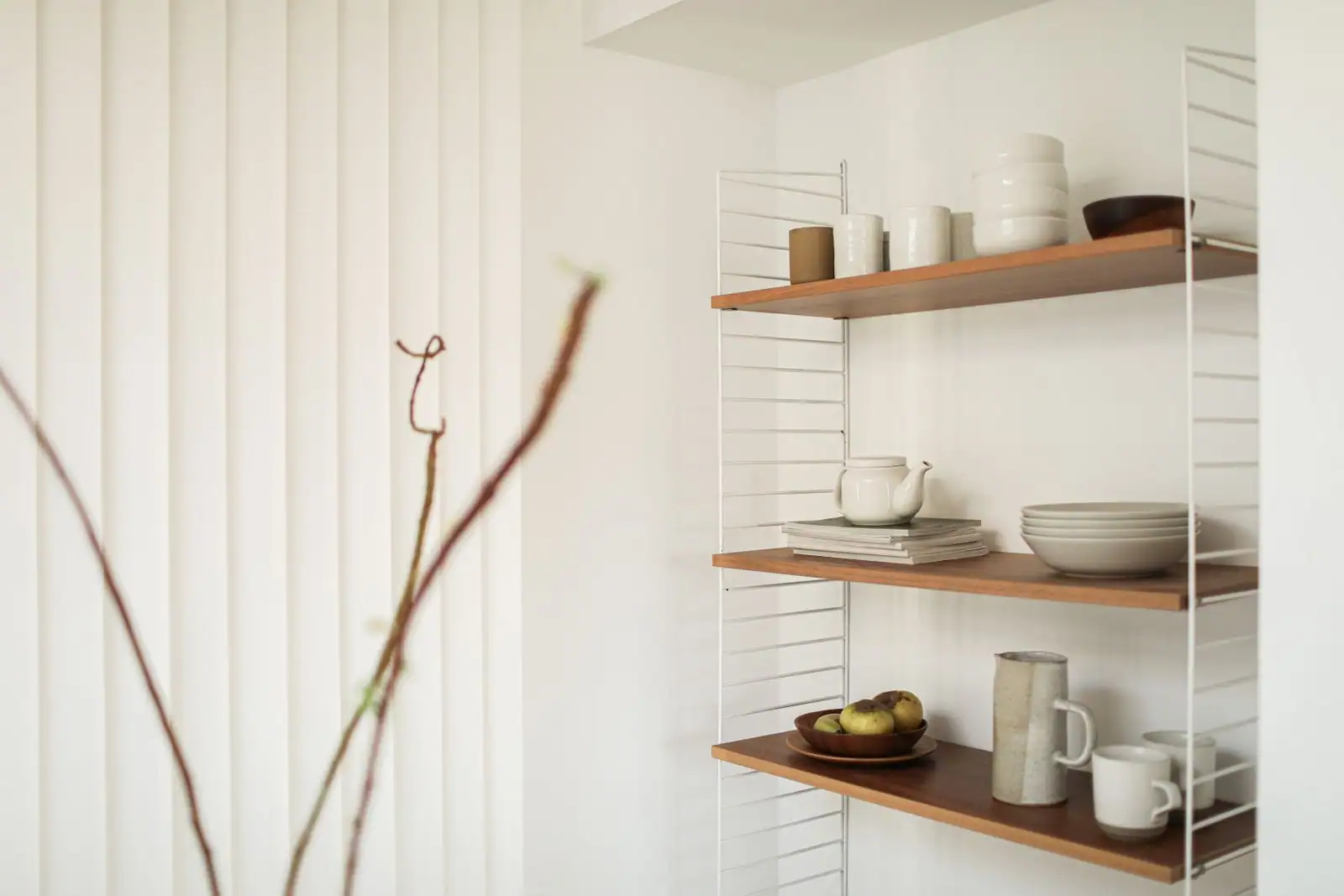 Vaisselle en céramique — bols, tasses, assiettes et théière — disposée sur des étagères en bois.