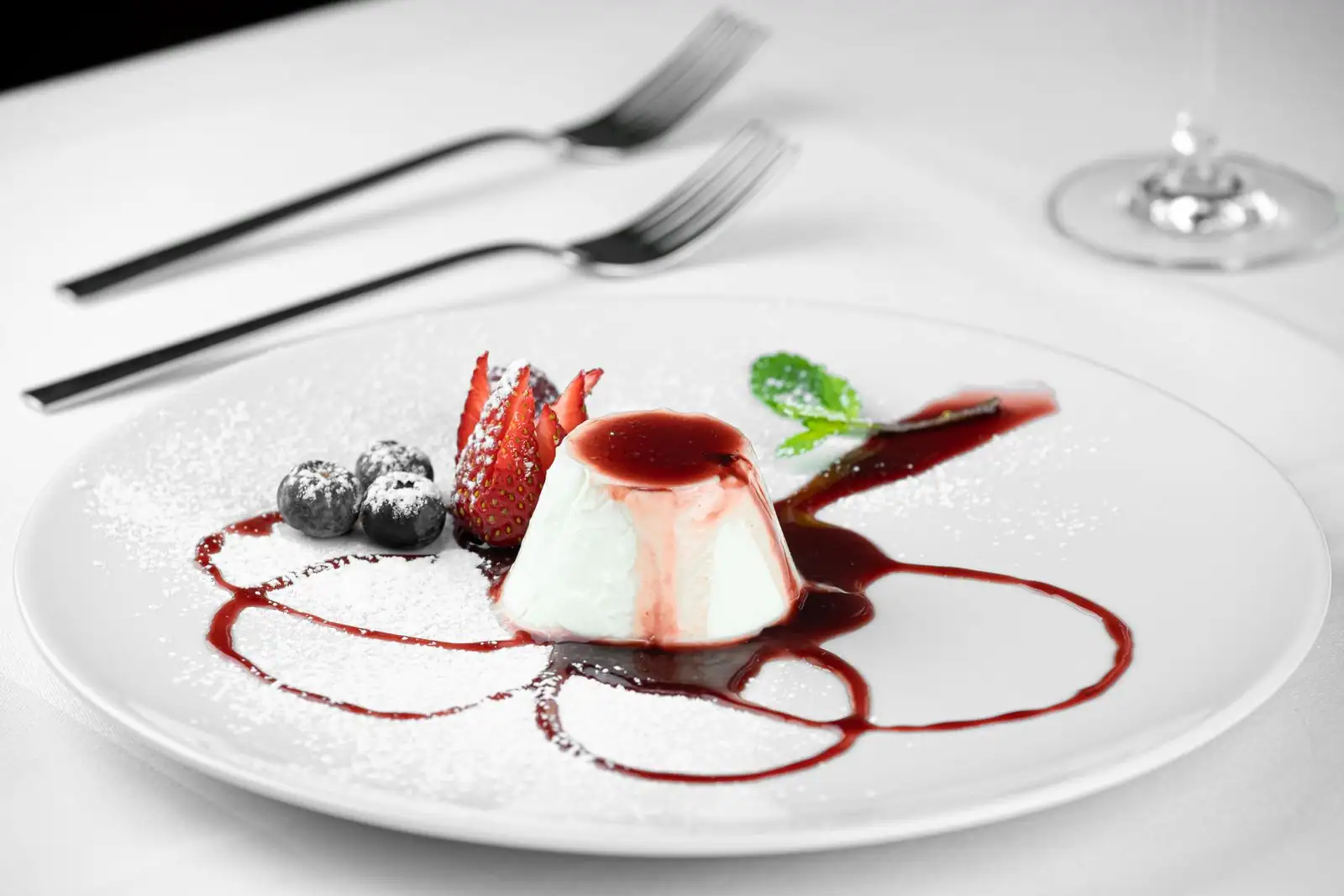 Panna cotta nappée de coulis de fruits rouges, garnie de fraises, de myrtilles et de menthe.