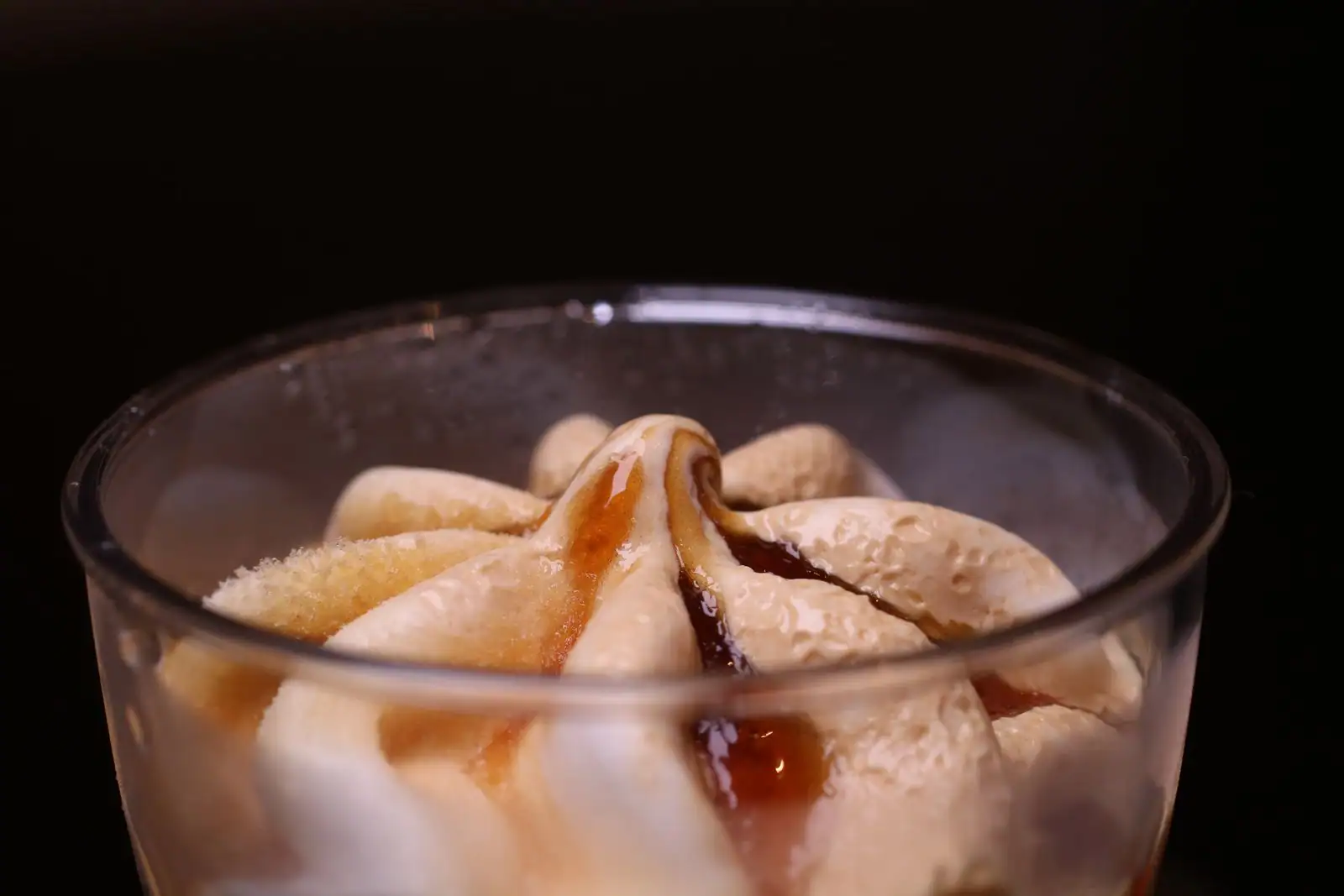 Glace vanille onctueuse nappée de sauce caramel, servie dans un verre sur fond sombre