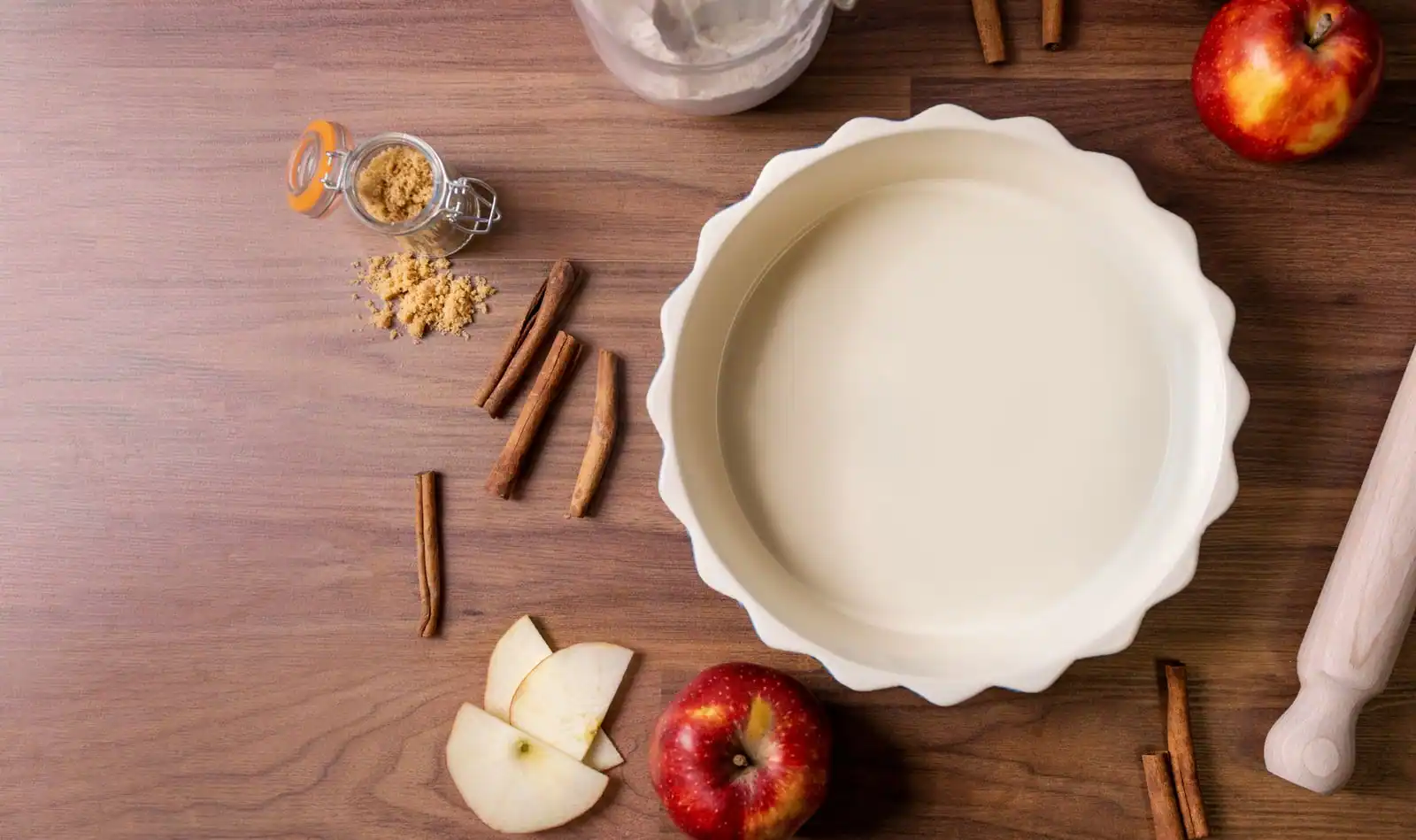 Pommes fraîches, cannelle et moule à tarte disposés sur une table en bois pour un dessert