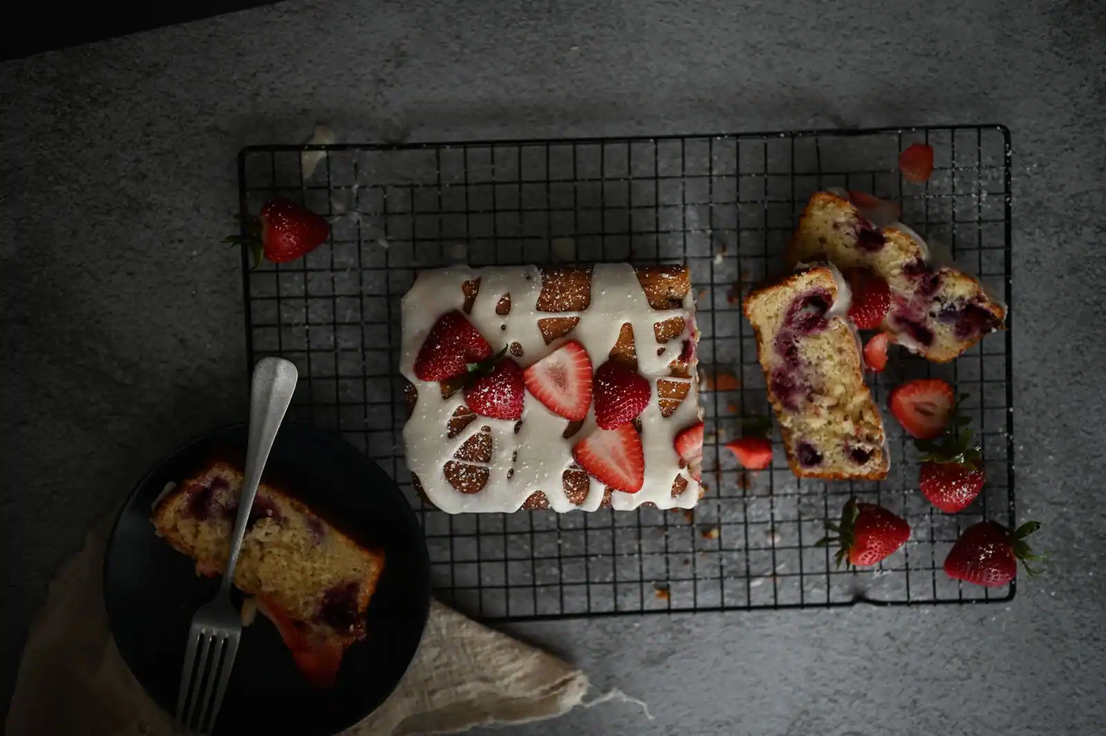 Gâteau glacé garni de fraises fraîches sur une grille, une part servie dans une assiette