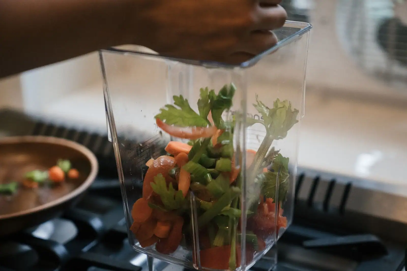 Blender de cuisine rempli de légumes frais — carottes, céleri, tomate et herbes — sur une cuisinière.
