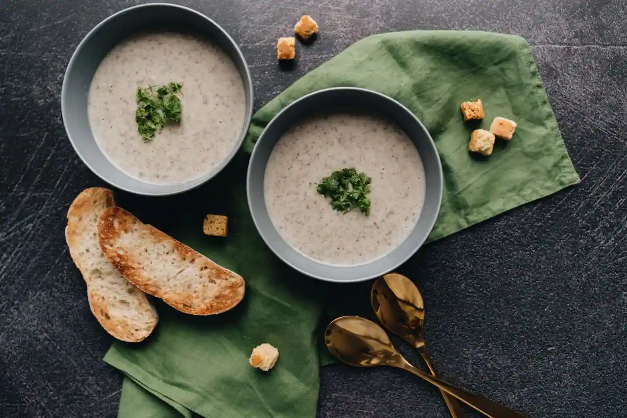 Deux bols de velouté crémeux garnis d'herbes, avec croûtons et pain grillé
