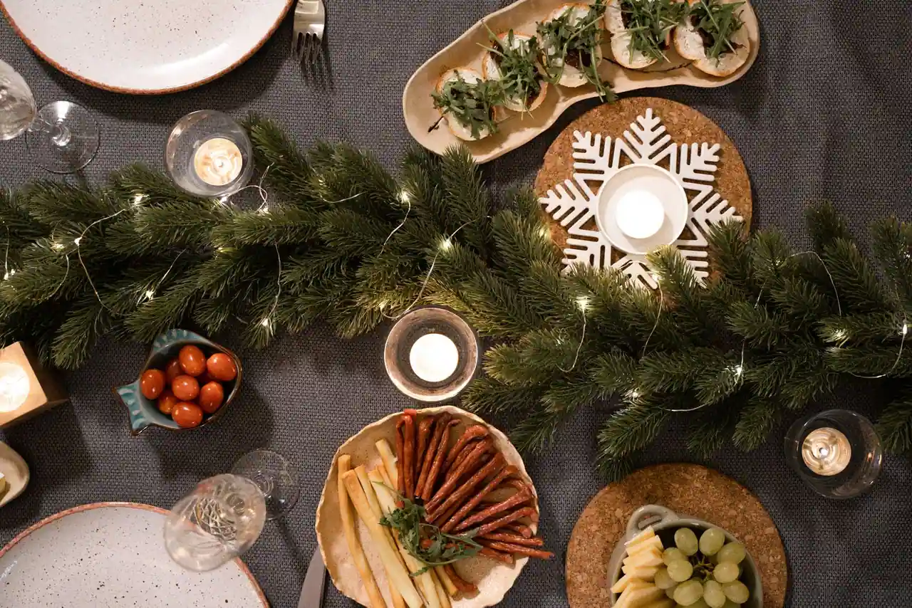 Table de fête de Noël vue de dessus, guirlande et bougies entourant des assiettes d'entrées et amuse-bouches