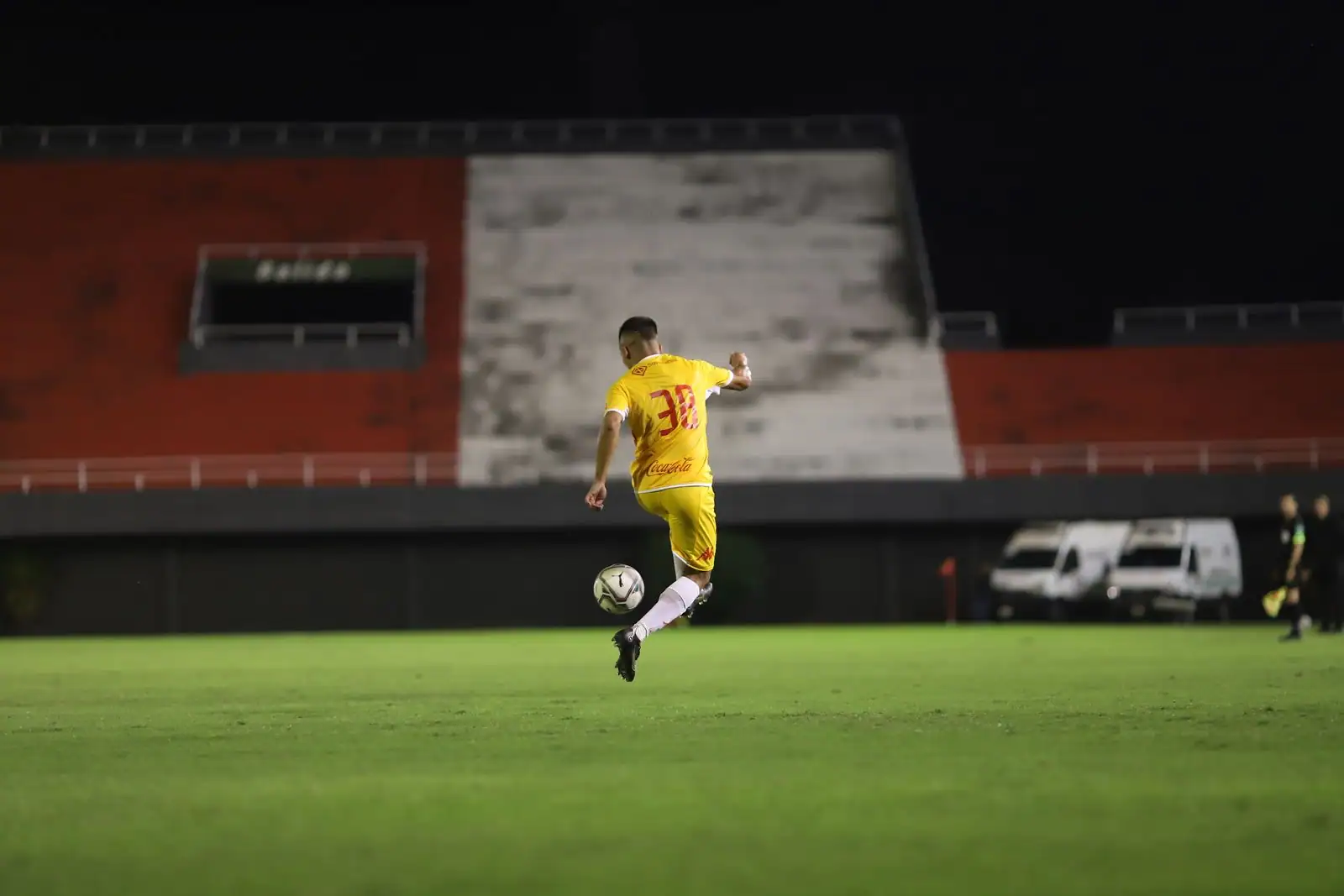 Footballeur en maillot jaune contrôlant le ballon sur la pelouse d'un stade en nocturne