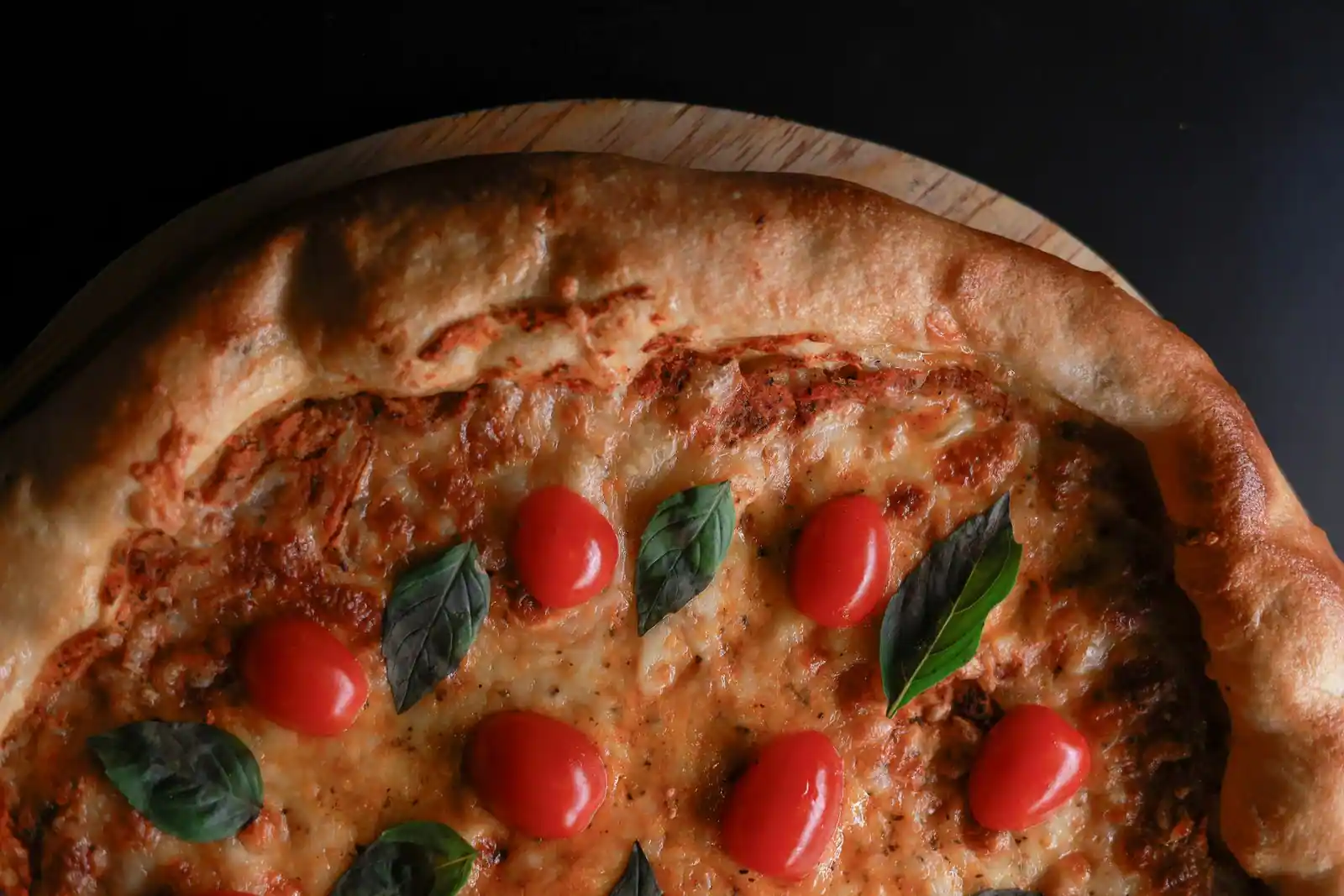 Gros plan d'une pizza maison cuite, fromage fondu, tomates cerises et basilic frais sur croûte dorée
