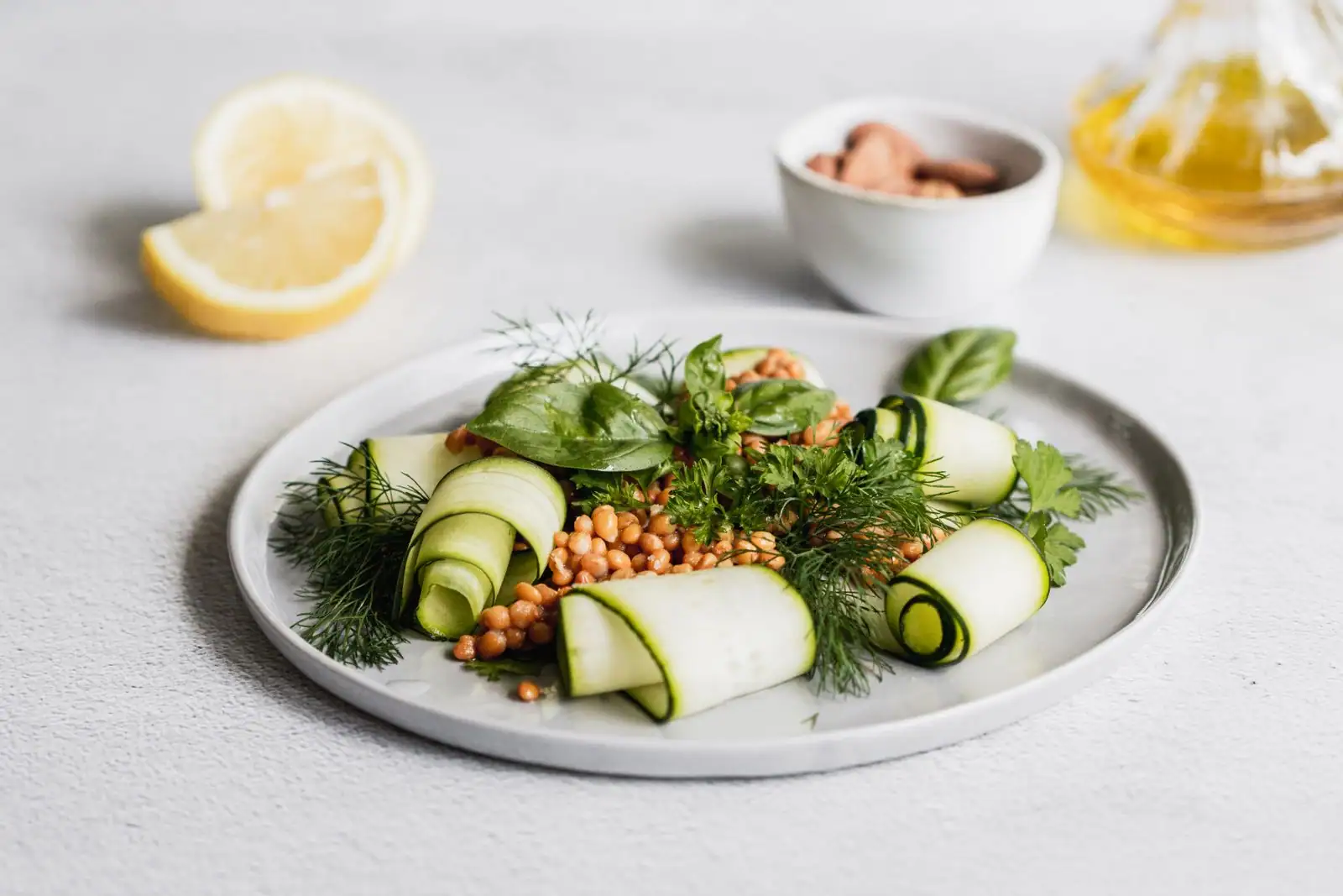 Assiette végétarienne de rubans de courgette, herbes fraîches et pignons, près d’un demi-citron
