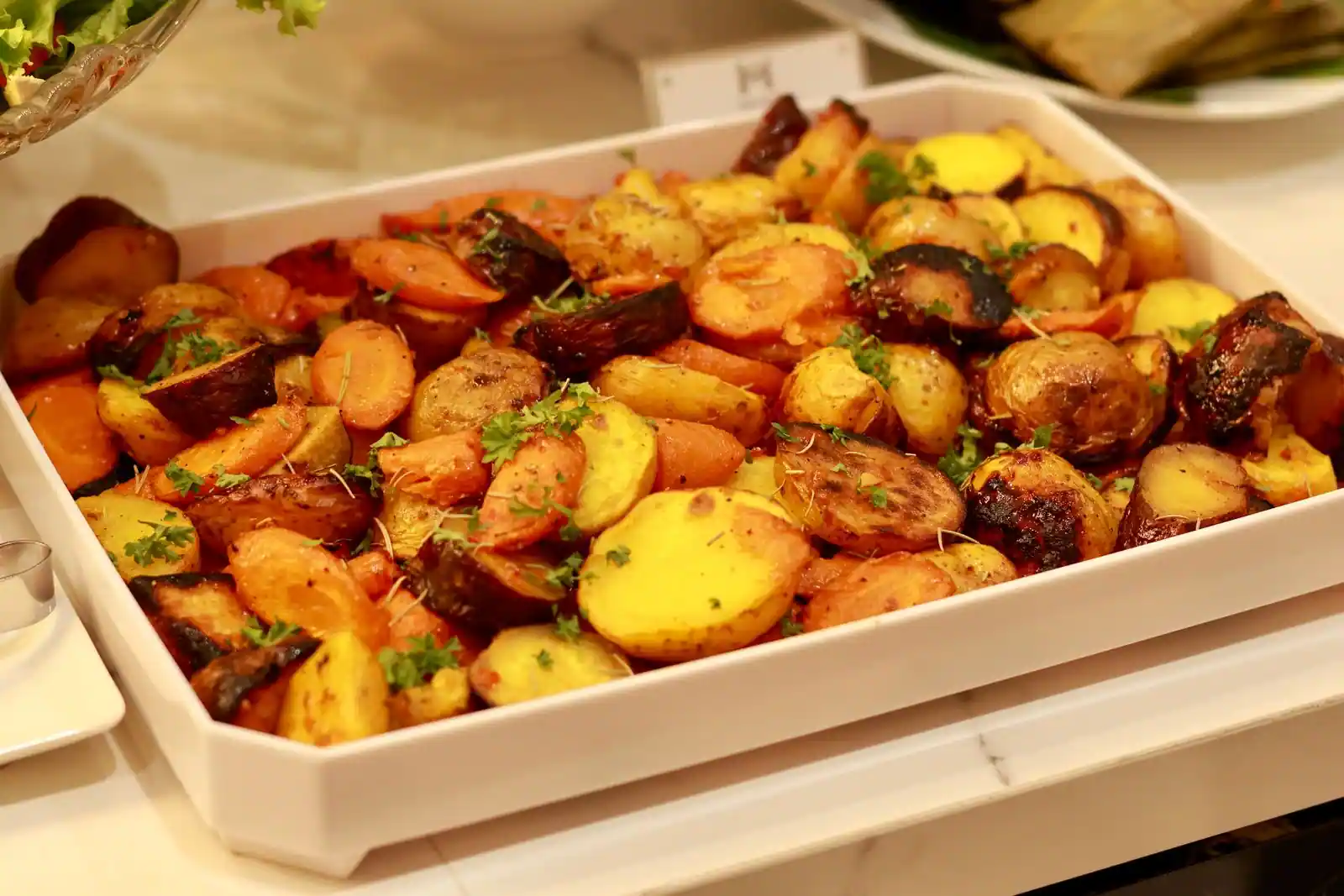 Plat de légumes rôtis dorés, pommes de terre et carottes, garni d'herbes fraîches