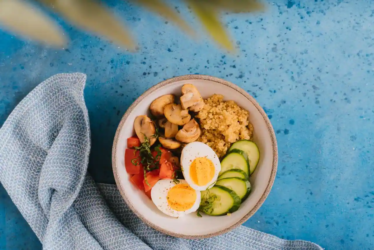 Bol healthy avec quinoa, champignons, tomate, concombre et œuf dur, dans un bol en céramique sur fond bleu