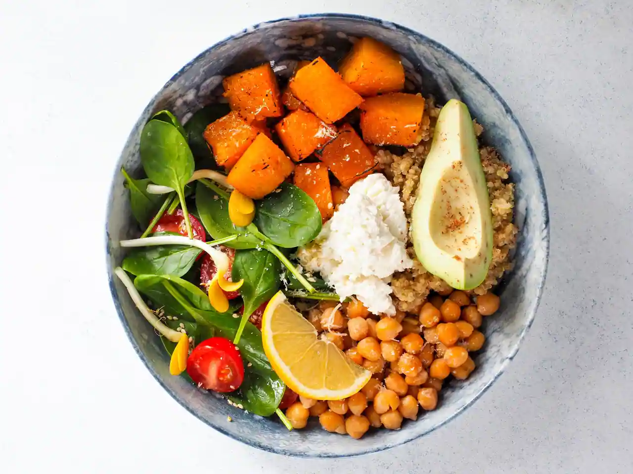 Bol végétarien composé de pois chiches, quinoa, courge rôtie, avocat et jeunes pousses