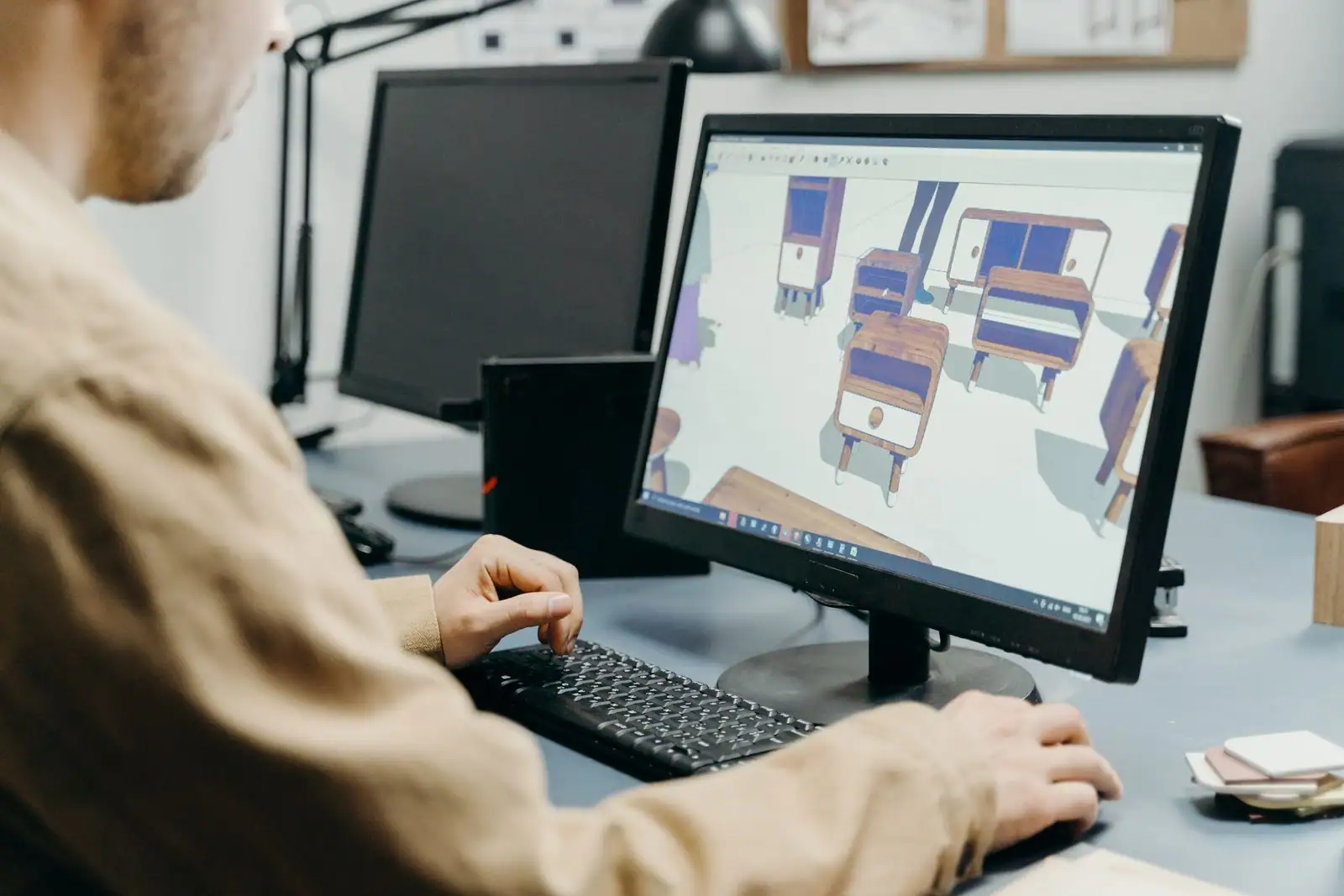 Personne travaillant sur un logiciel de modélisation 3D, des objets en trois dimensions affichés à l'écran