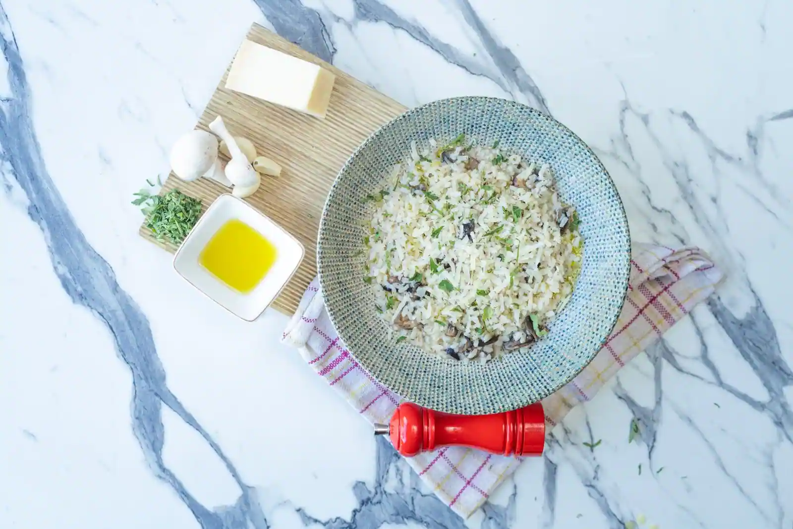 Bol de risotto aux champignons, grains de riz et herbes visibles, parmesan et huile d'olive à côté