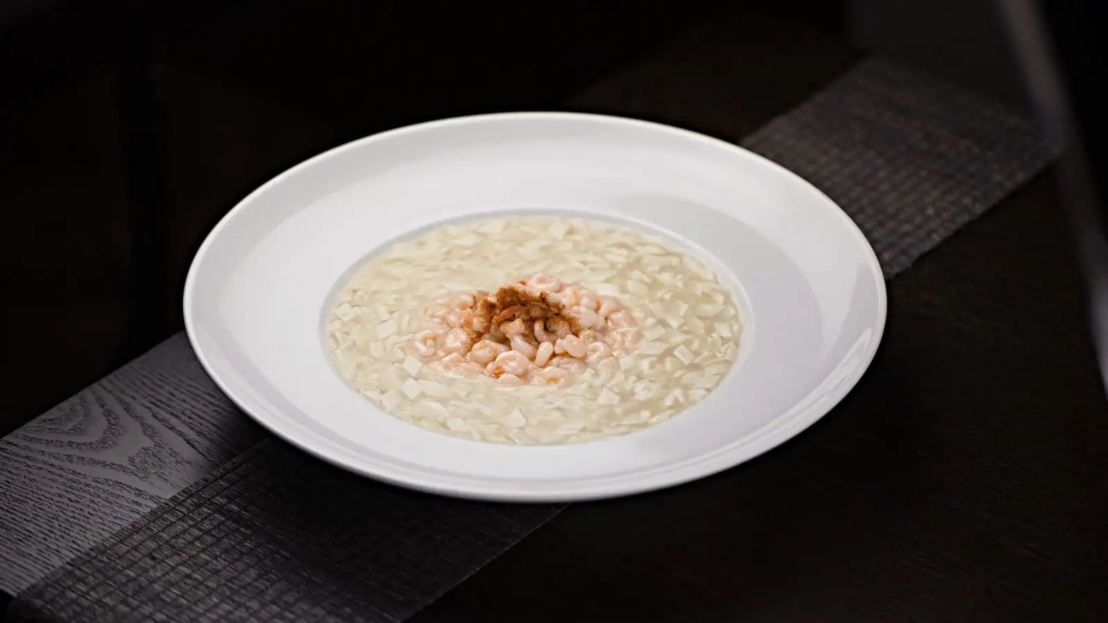 Assiette de risotto crémeux garni de petites crevettes, sur une table en bois sombre