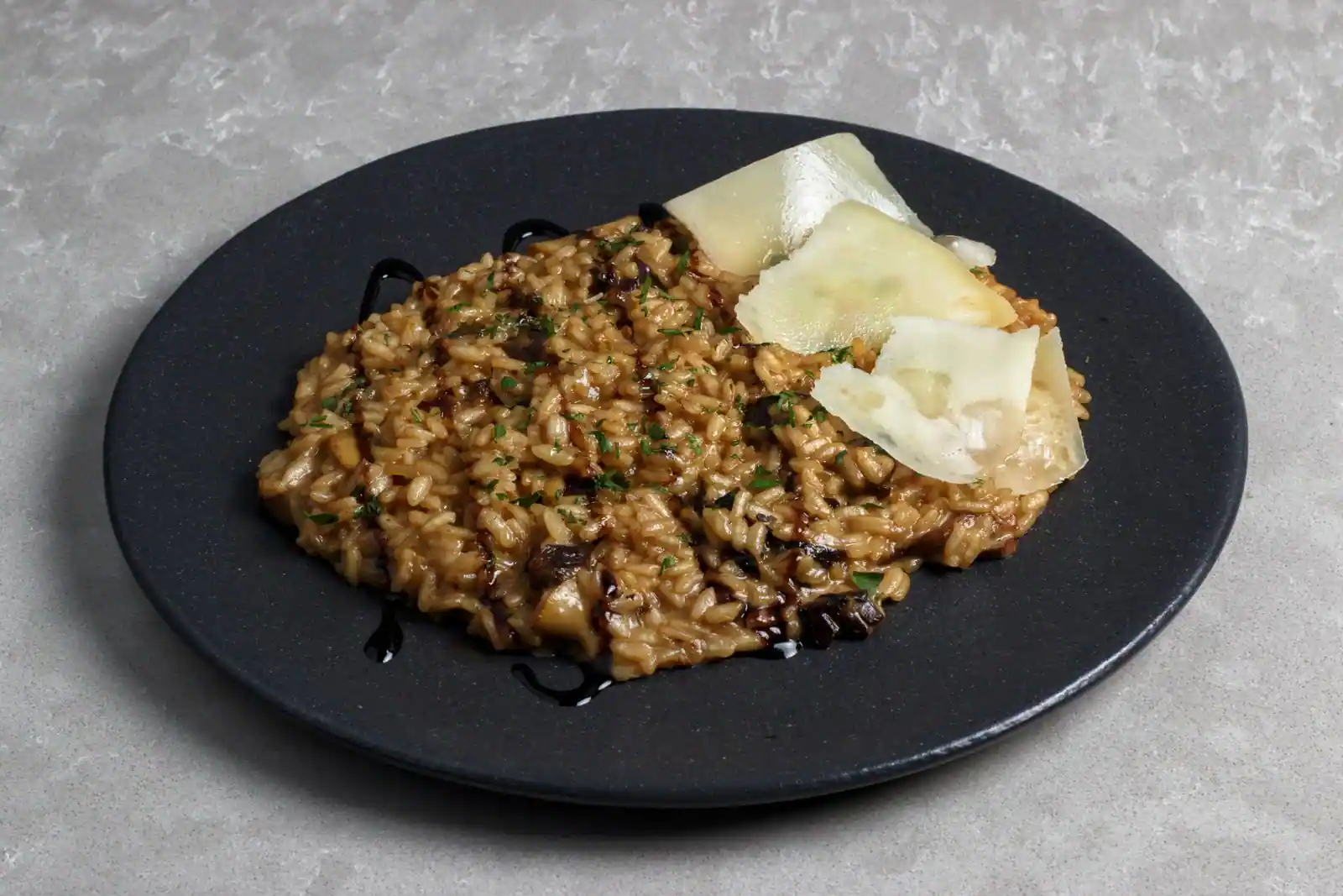 Risotto aux champignons servi sur une assiette noire, copeaux de parmesan et persil