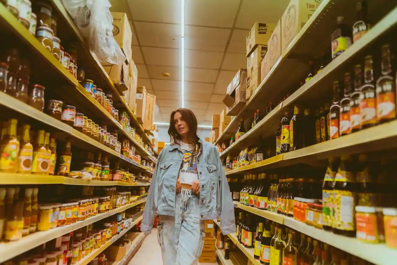 Jeune femme debout dans une allée d'épicerie bordée d'étagères de produits emballés