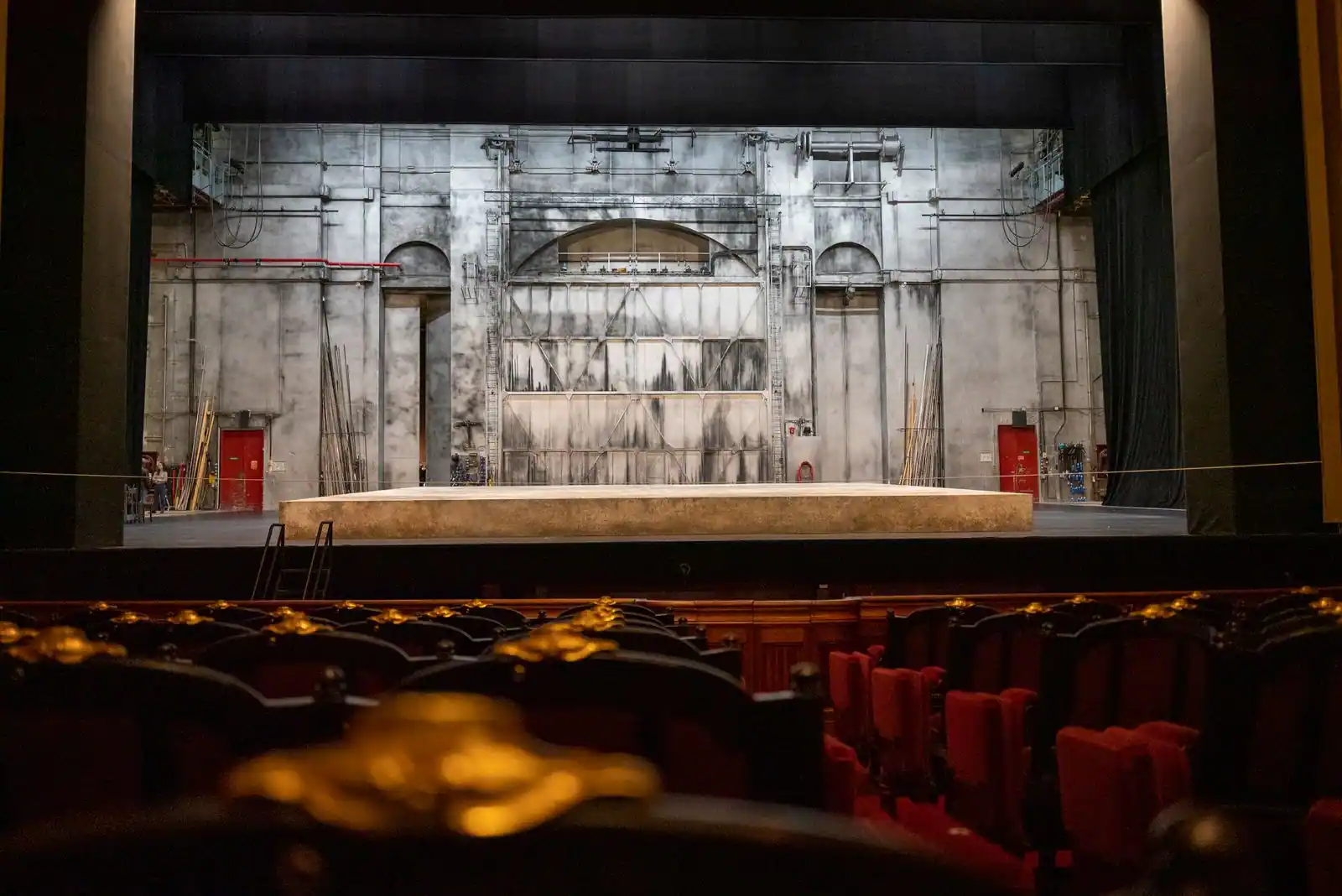 Scène de théâtre vue depuis la salle, avec fauteuils de velours rouge au premier plan