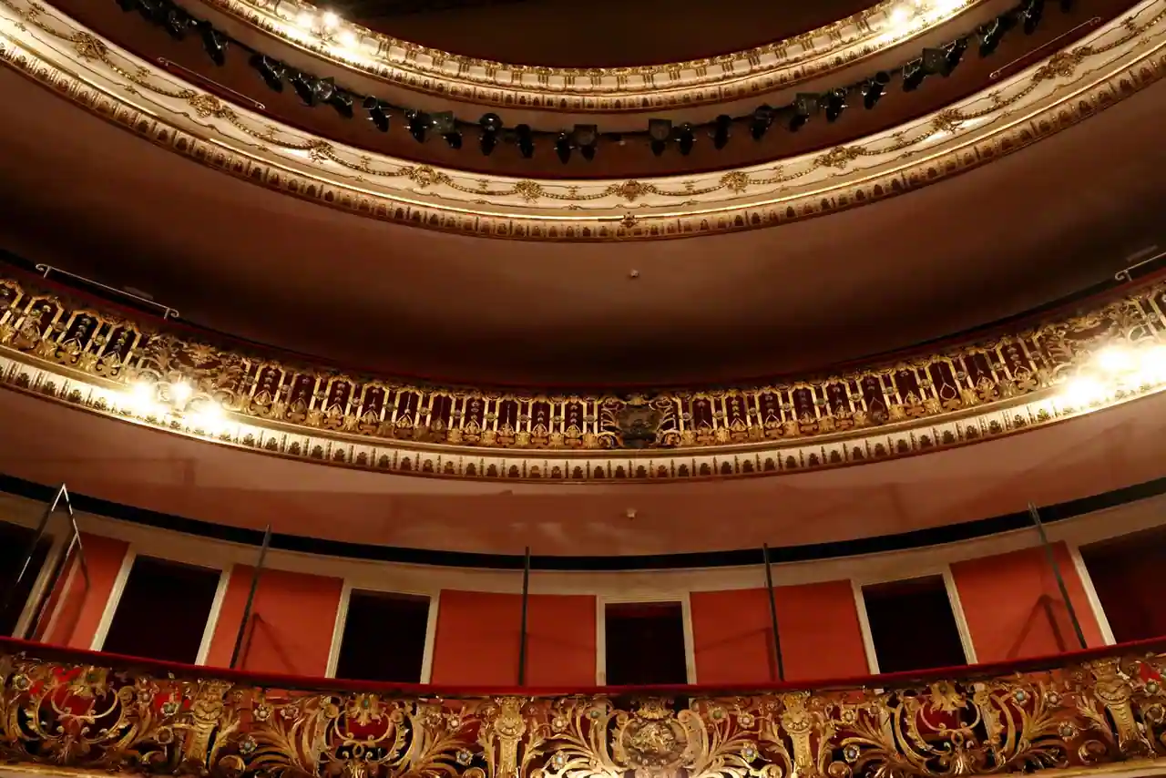 Balcons dorés à l'italienne d'une salle de théâtre, avec loges tendues de rouge sur plusieurs niveaux.