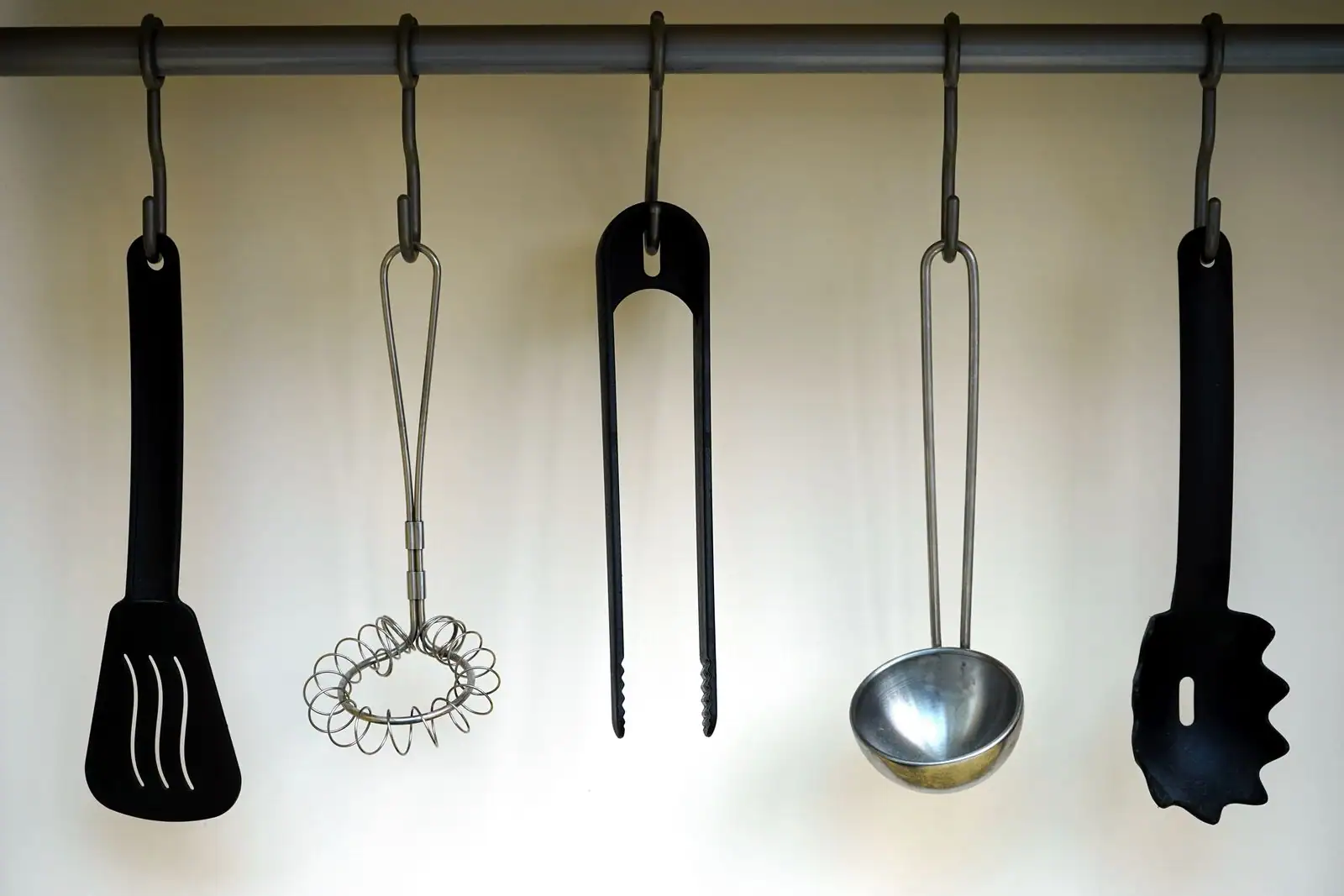 Ustensiles de cuisine suspendus à une barre : spatule, louche, pince et cuillère à pâtes