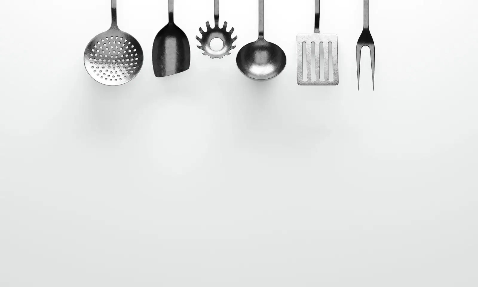 Série d'ustensiles de cuisine en inox alignés sur fond clair
