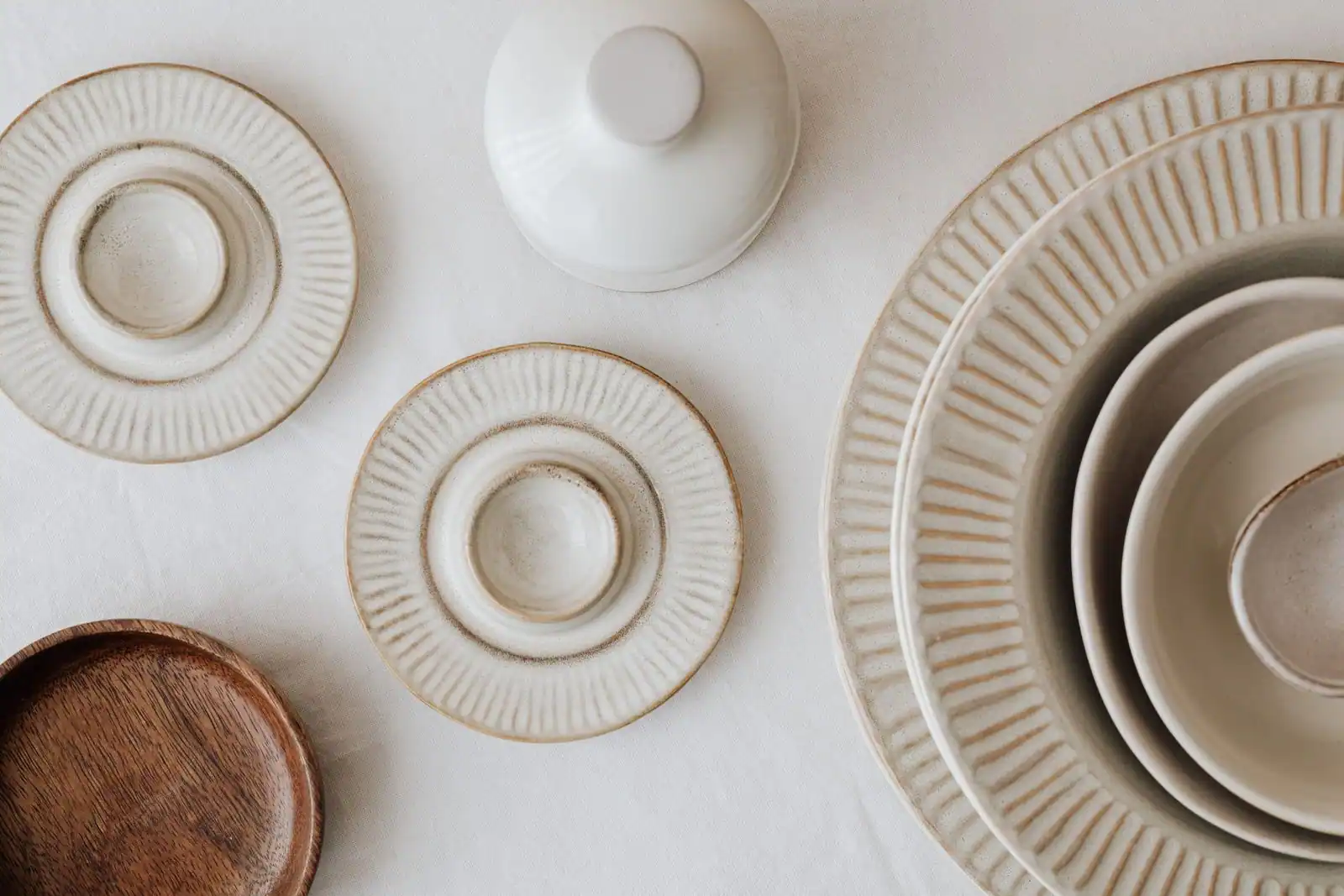 Assiettes en grès aux tons crème et beige à la finition mate, avec un plat en bois clair, vues de dessus.