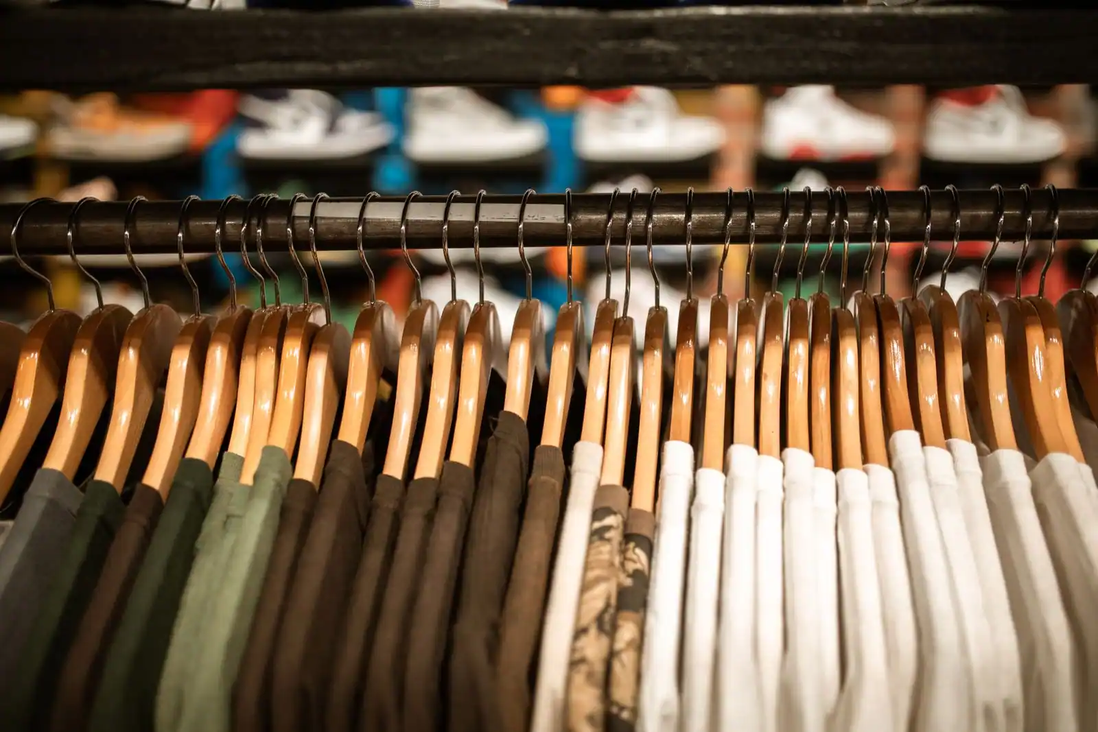 Vêtements suspendus sur des cintres en bois le long d'un portant, paires de baskets en rayon à l'arrière