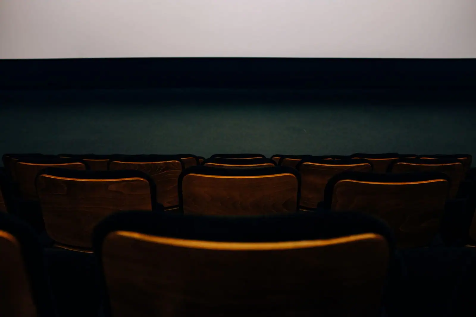 Rangées de fauteuils en bois dans une salle de cinéma plongée dans la pénombre