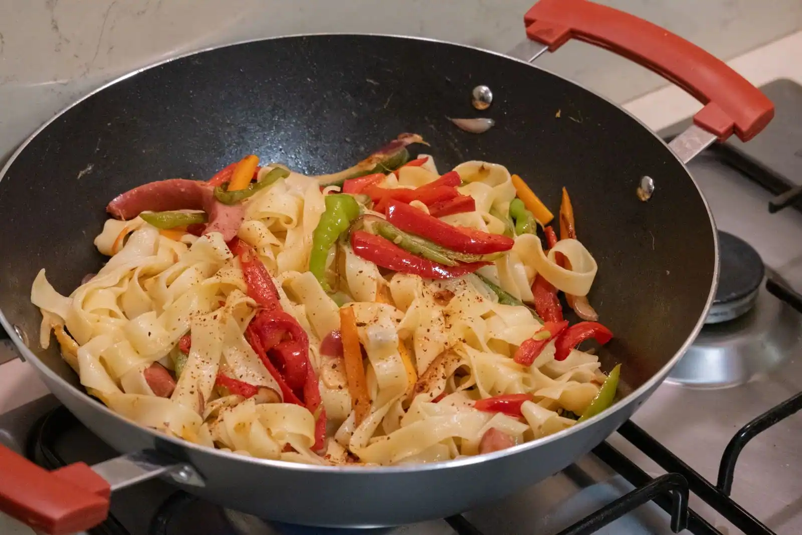 Wok garni de nouilles plates et de lamelles de poivrons et de carottes, posé sur une cuisinière