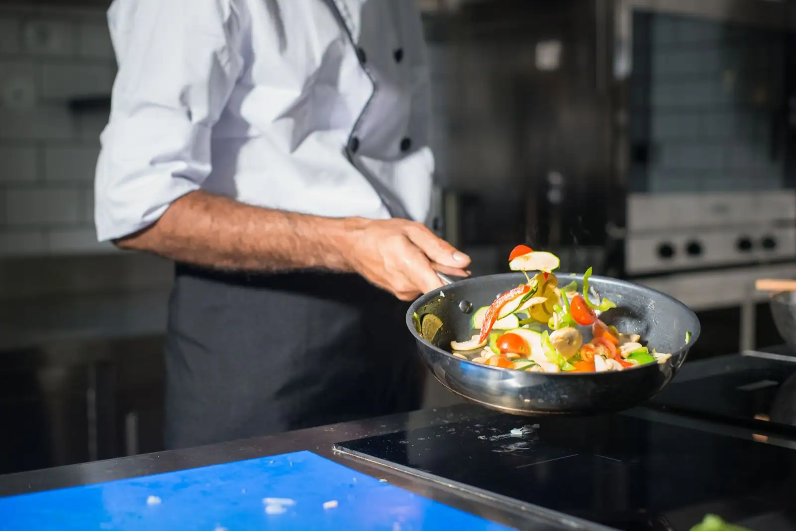Cuisinier saisissant des légumes colorés dans une poêle, dans la cuisine d'un restaurant.