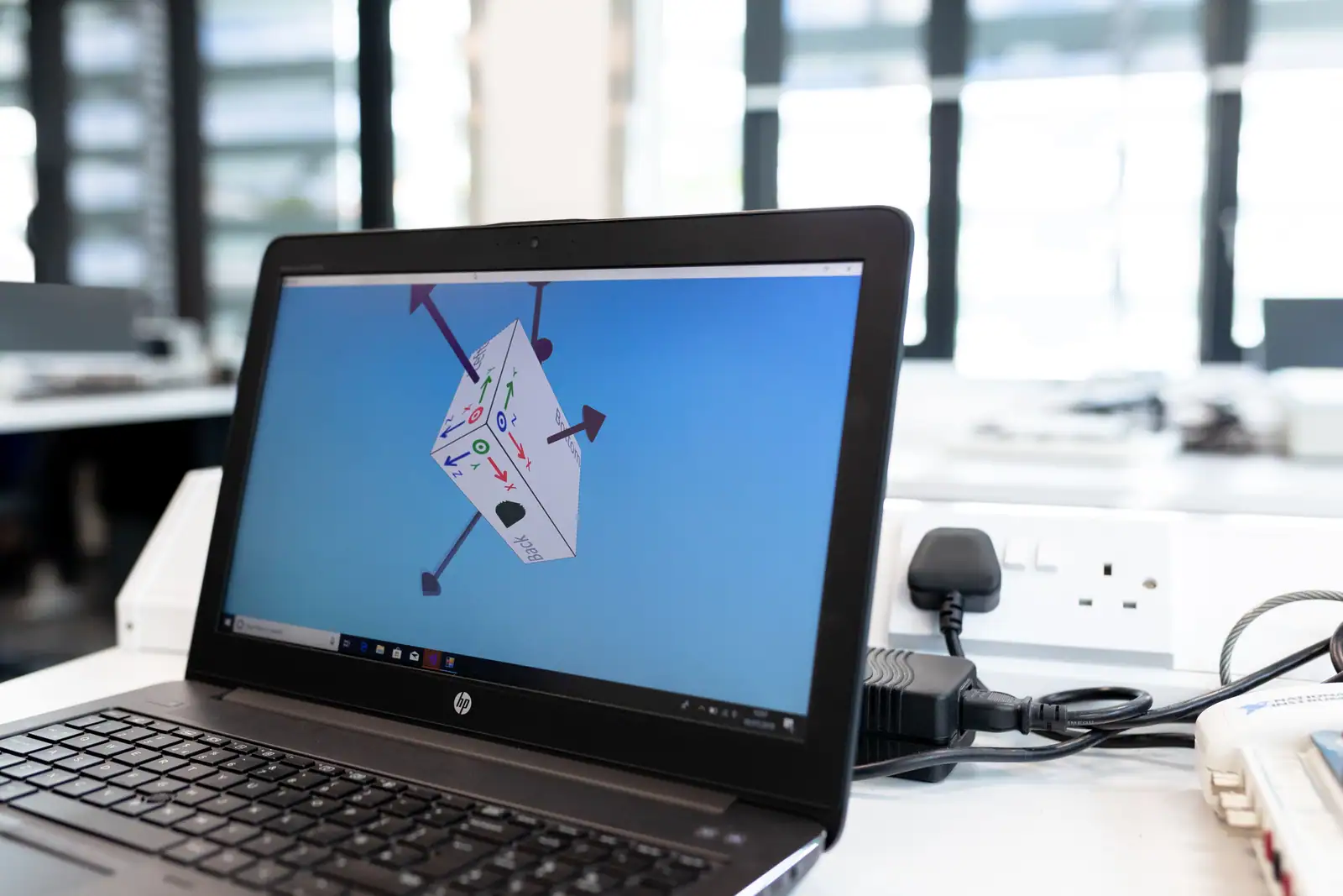 Ordinateur portable affichant un objet 3D et ses axes d'orientation dans un logiciel de modélisation.