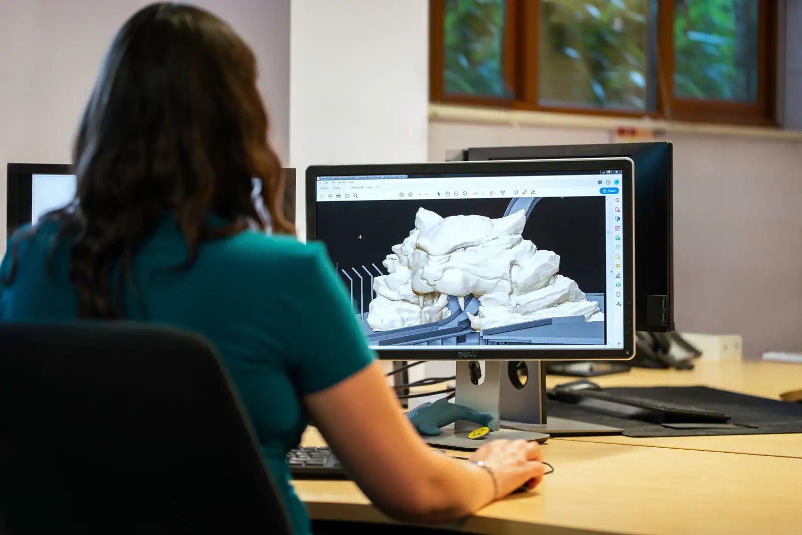 Personne travaillant devant un écran d'ordinateur qui affiche un modèle 3D blanc, sans texture