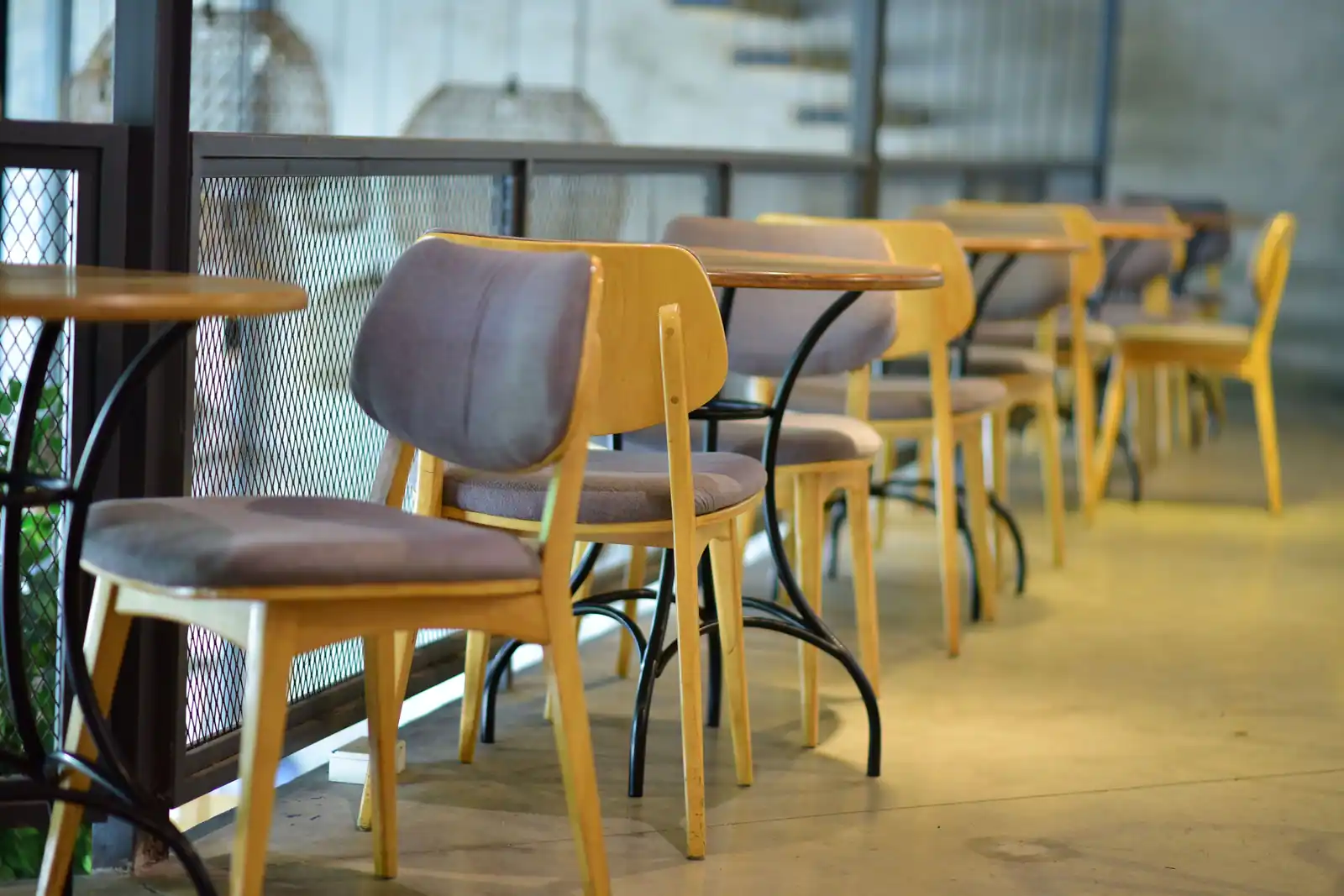Rangée de chaises en bois et de petites tables le long d'une balustrade métallique, salle sobre