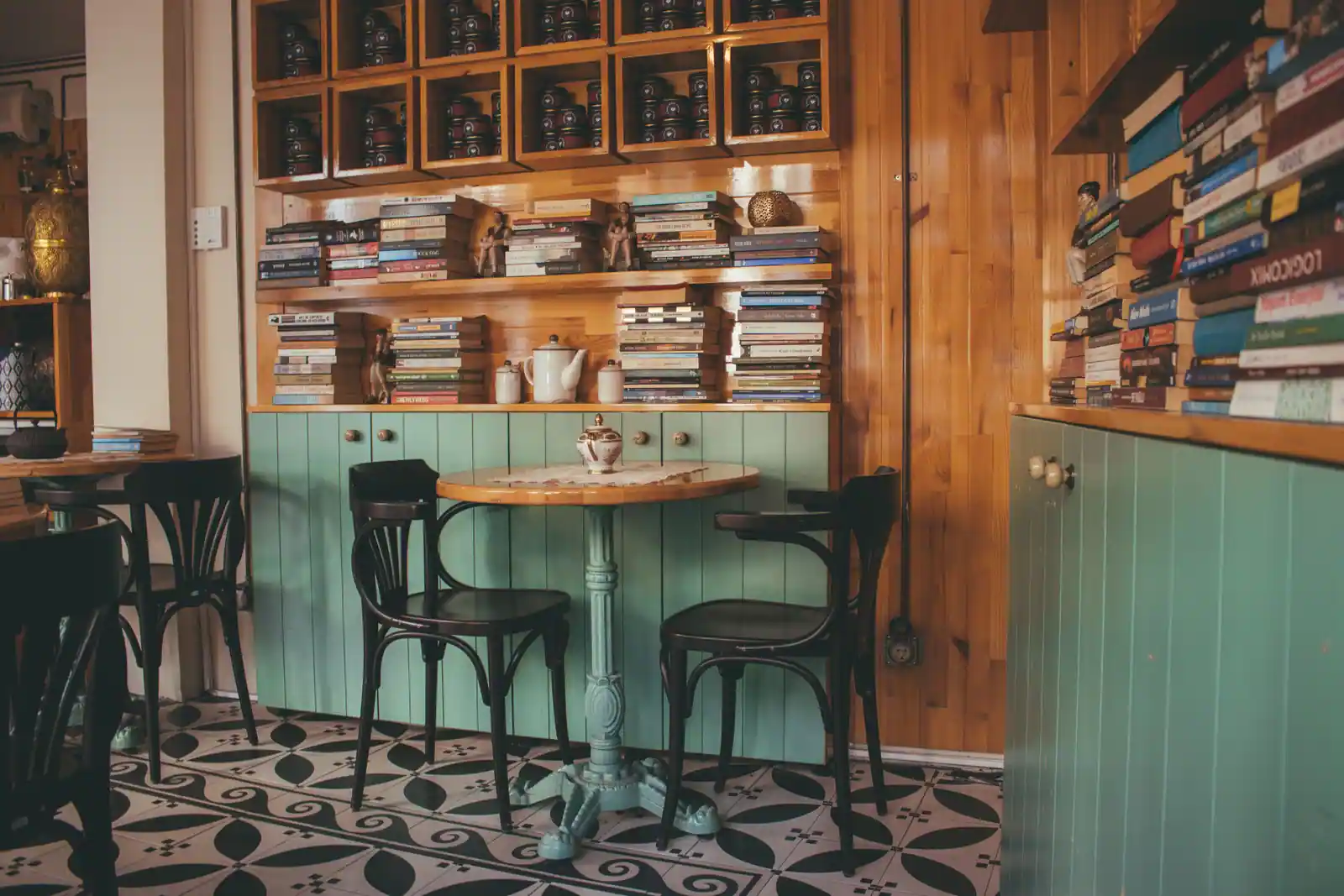 Salle de café aux murs couverts de livres empilés, avec une table ronde de bistrot et des chaises en bois