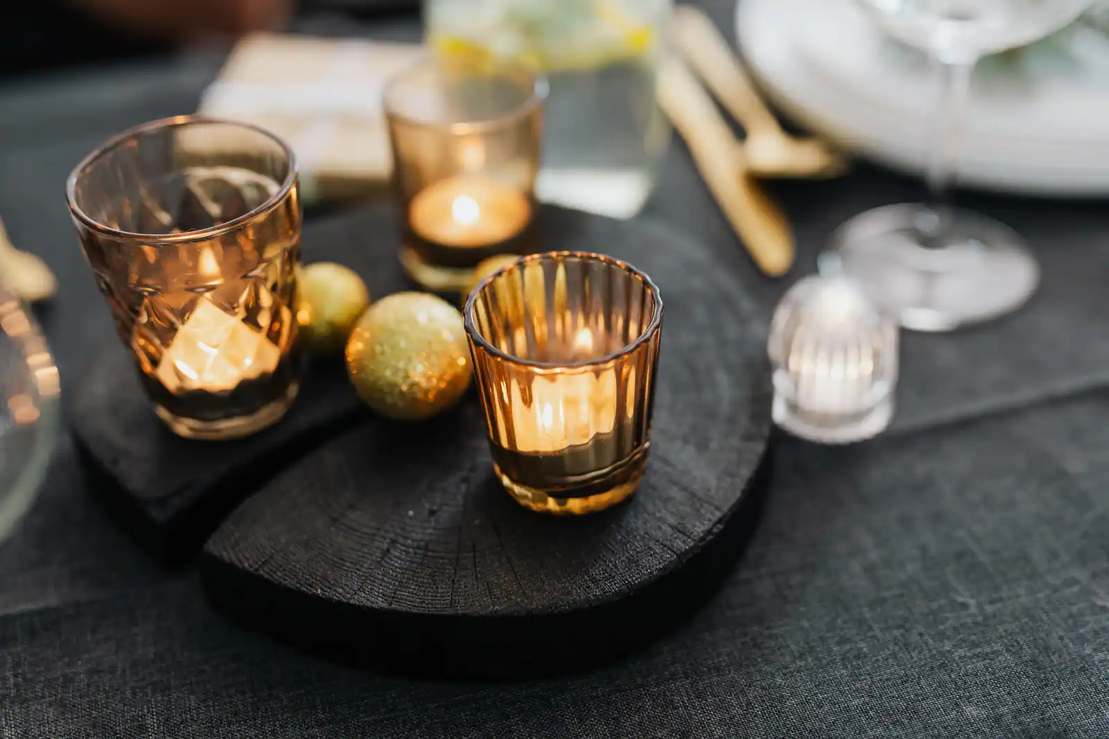 Photophores en verre ambré et boules dorées posés sur une nappe noire, à la lueur des bougies