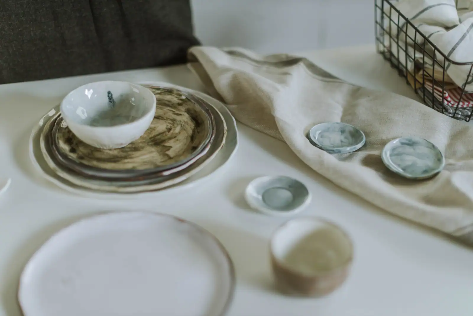 Assiettes en céramique artisanale, coupelles émaillées et linge en lin posés sur une surface claire.
