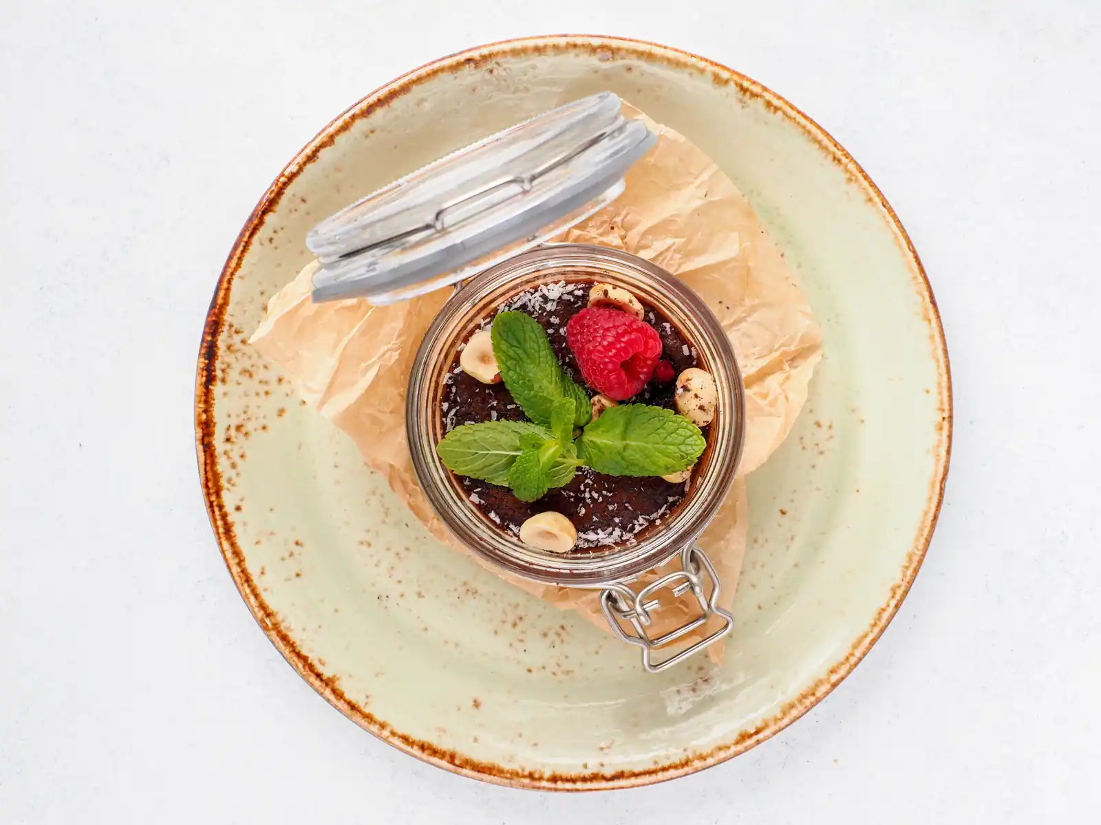 Dessert au chocolat servi en bocal, garni d'une framboise, de menthe, de noisettes et de coco râpée