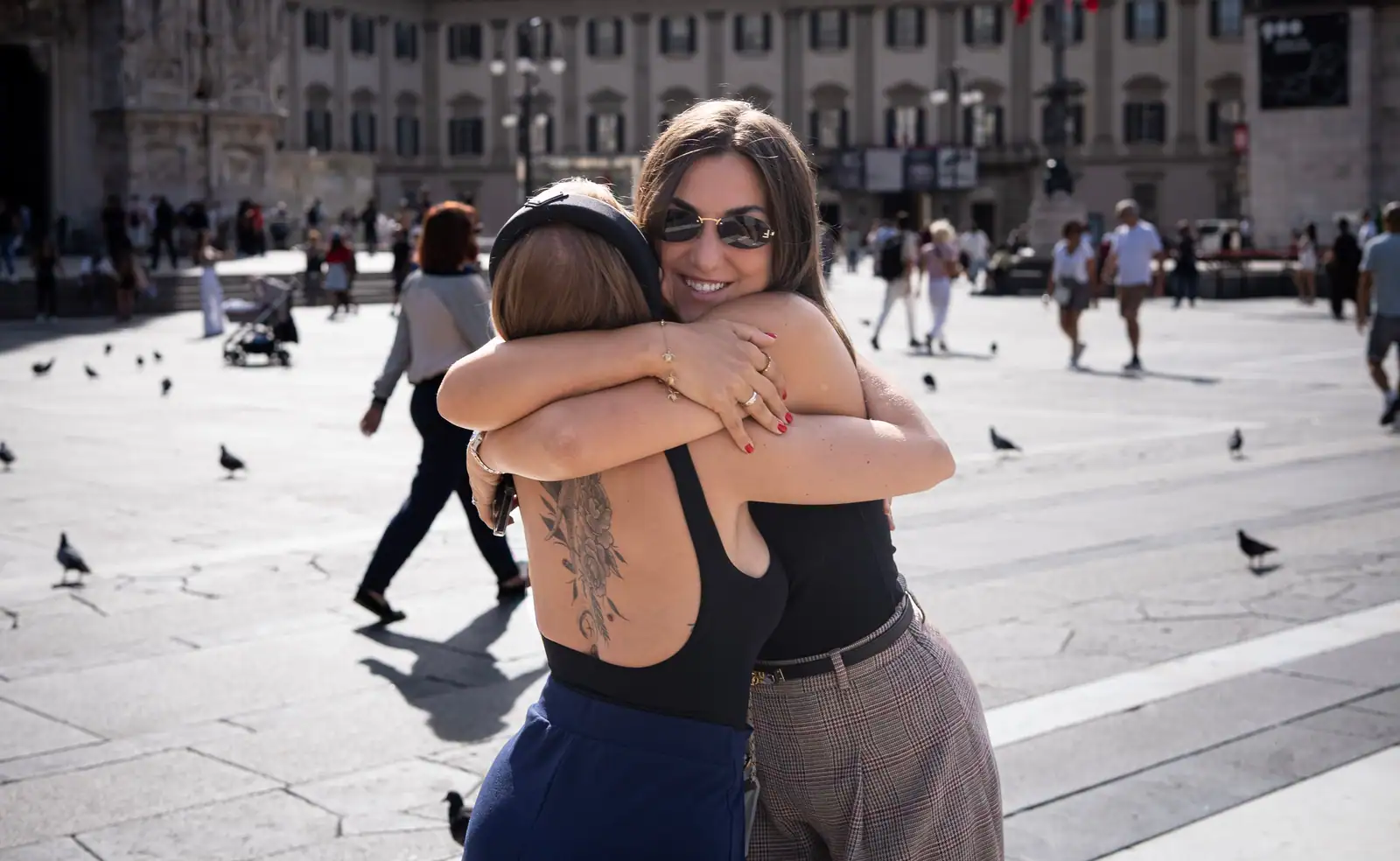 Deux femmes s'étreignent sur la place du Duomo à Milan, au milieu des passants et des pigeons