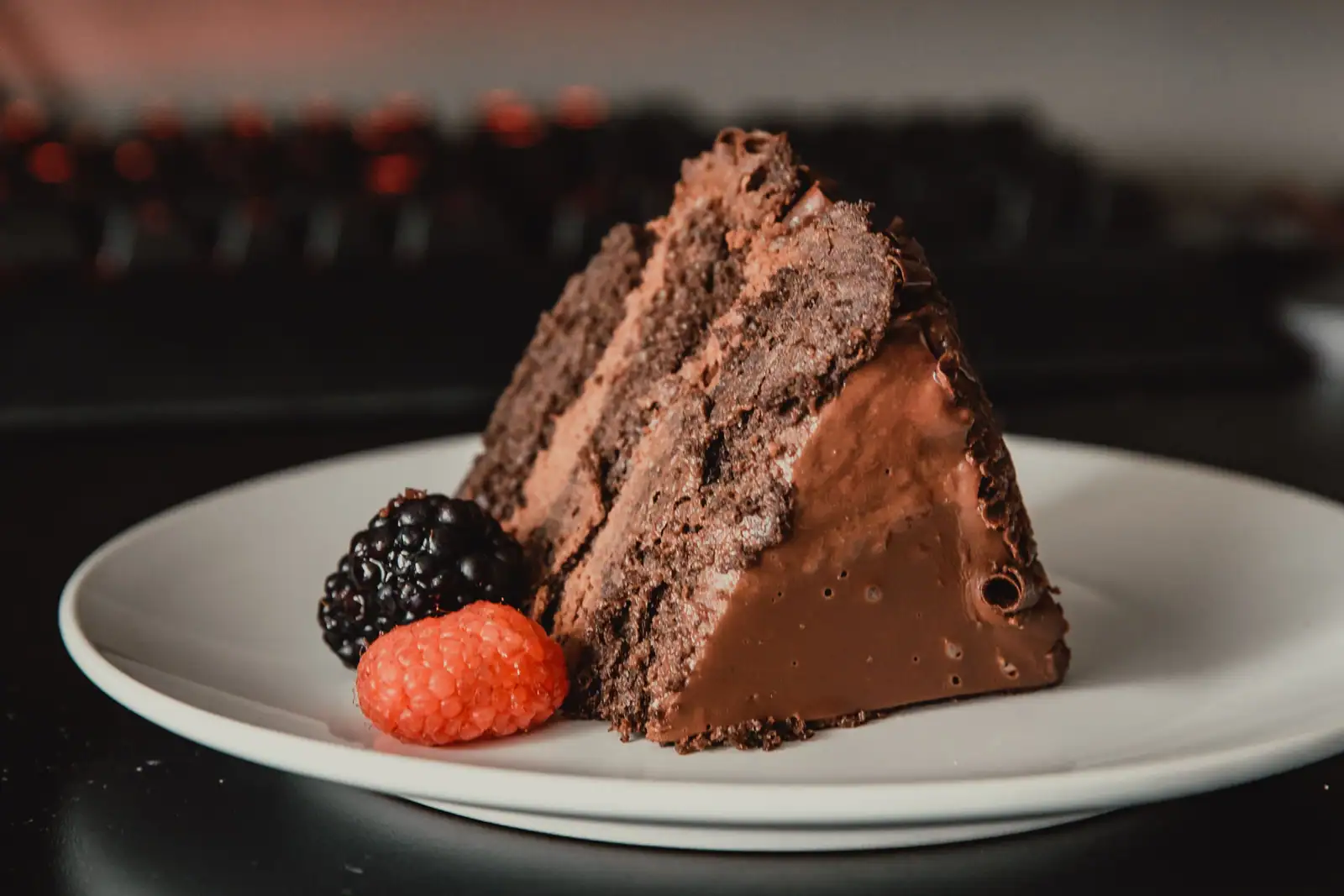 Part de gâteau au chocolat à étages nappée d'un glaçage lisse, servie avec une mûre et une framboise