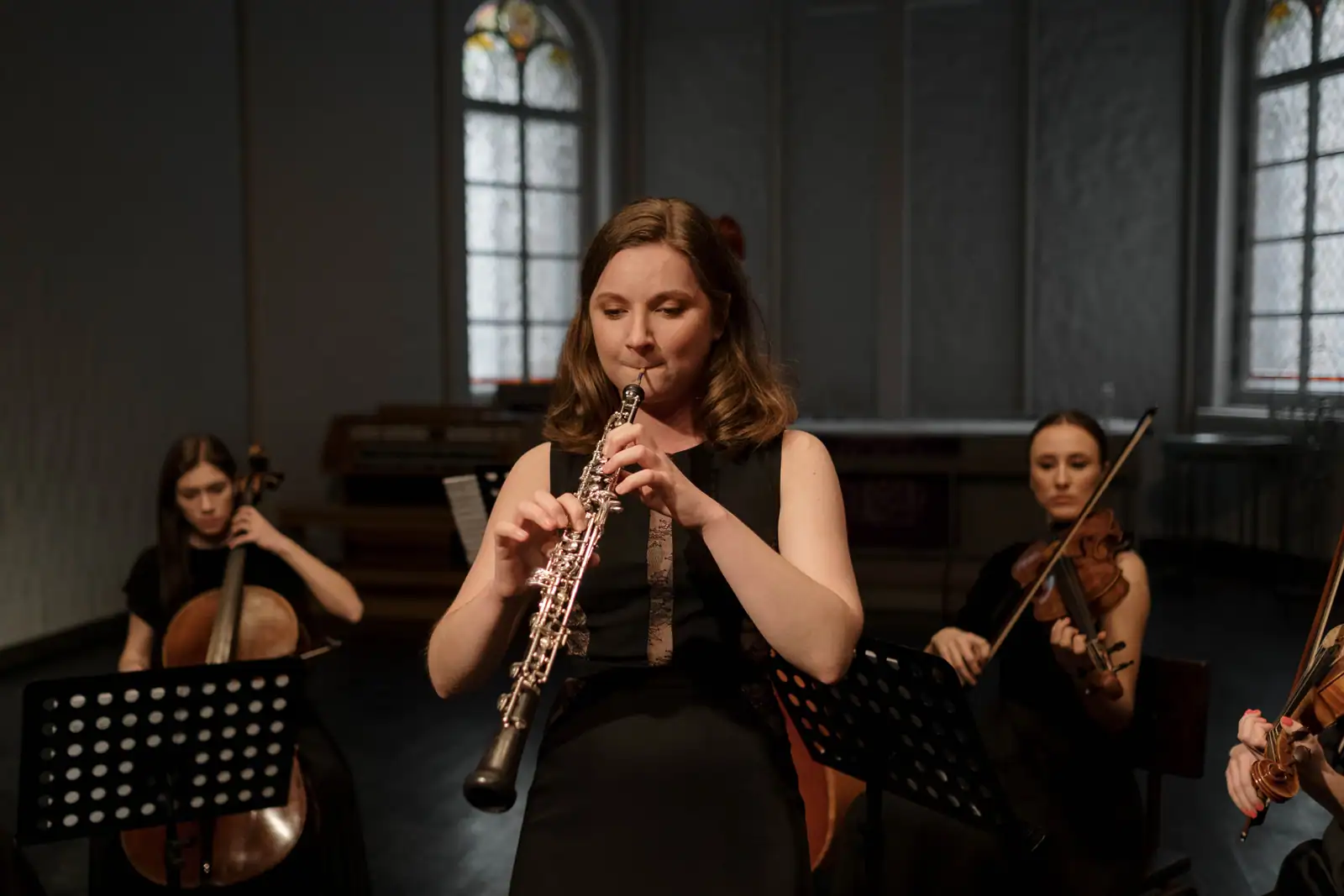 Une musicienne joue du hautbois au sein d'un petit ensemble, un violoncelle et un violon derrière elle
