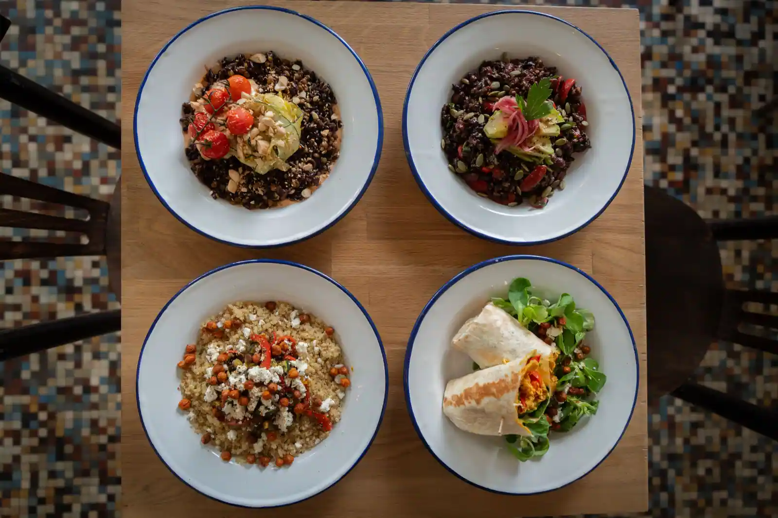 Quatre bols de repas végétariens vus du dessus : céréales, légumineuses, légumes et wrap sur une table en bois